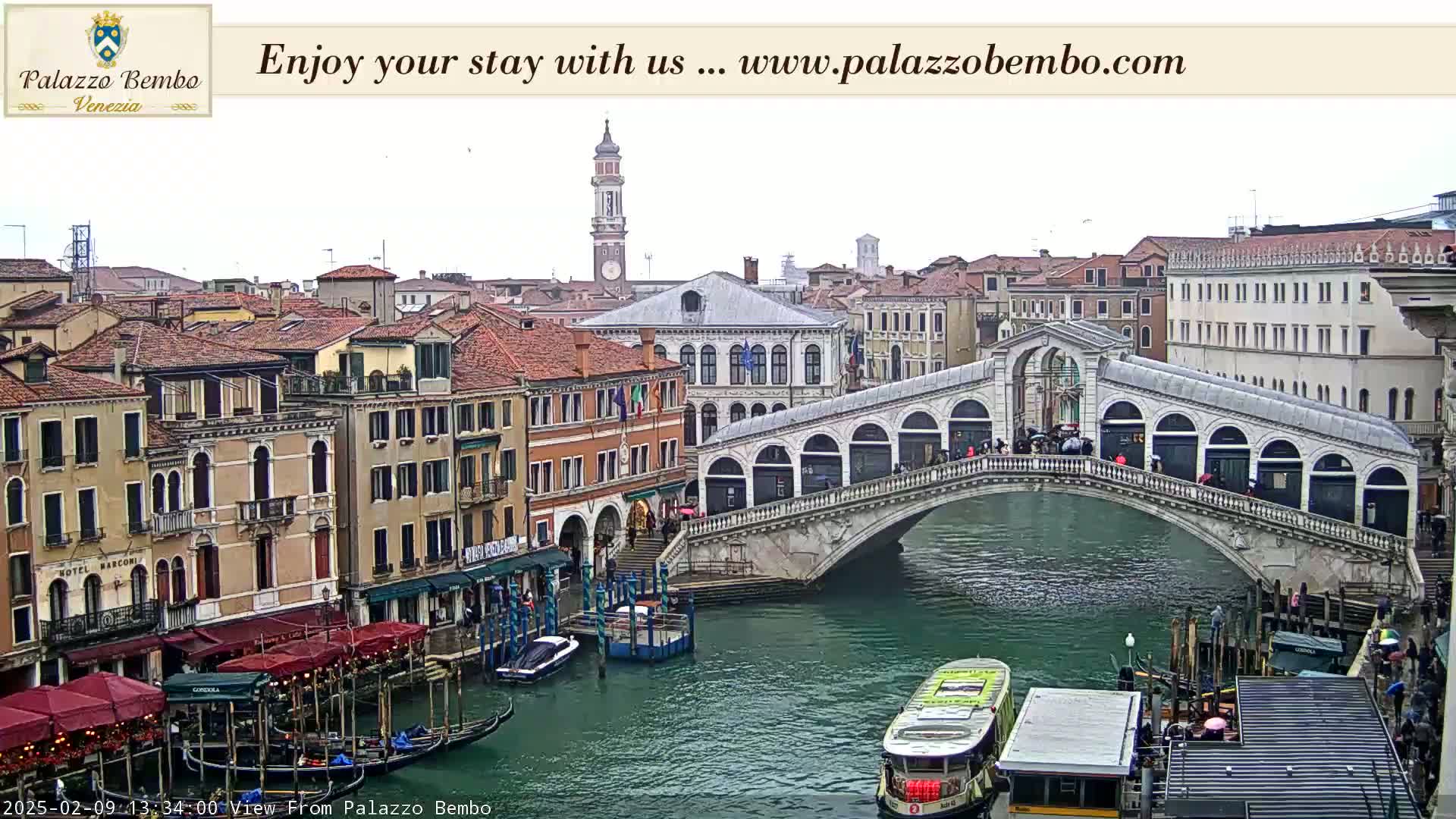 A view of a canal in Venice, showing a bridge with pedestrians, gondolas, and buildings on either side under an overcast sky.