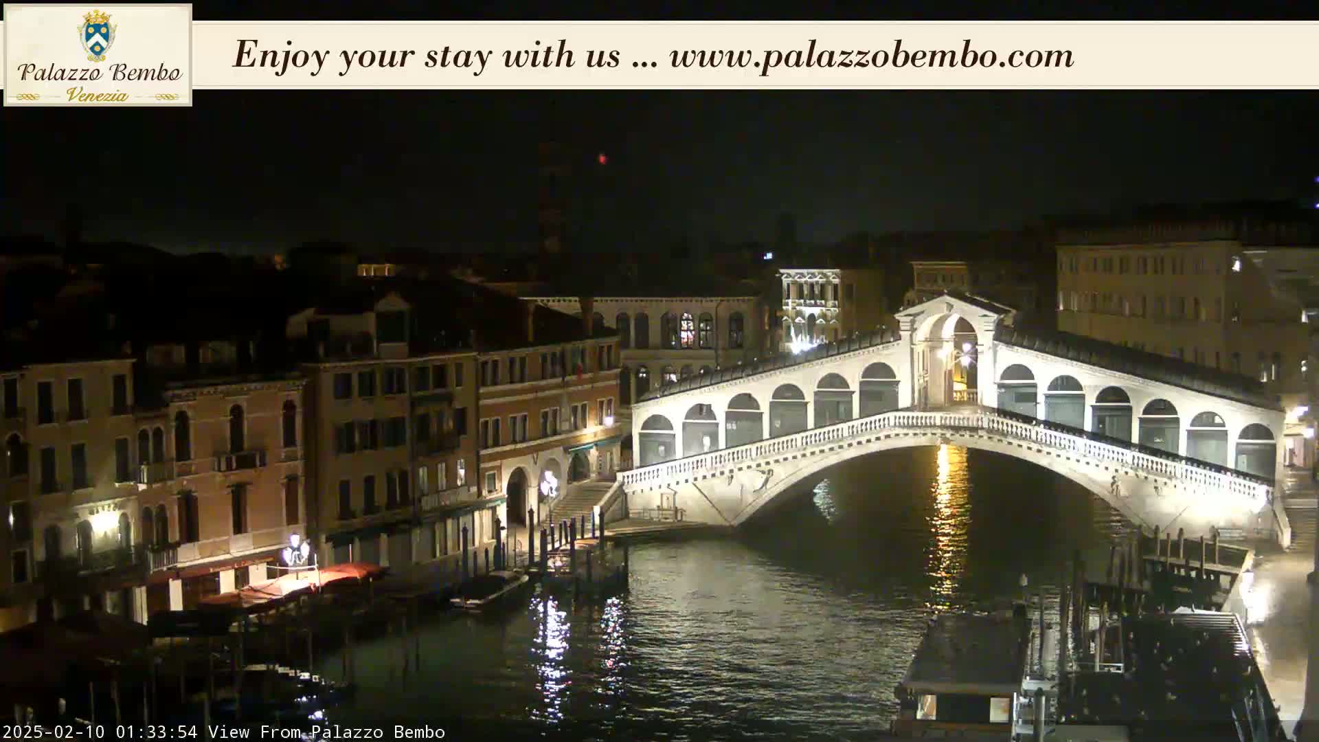 A nighttime view of a bridge over a canal in Venice, with illuminated buildings lining the waterway.