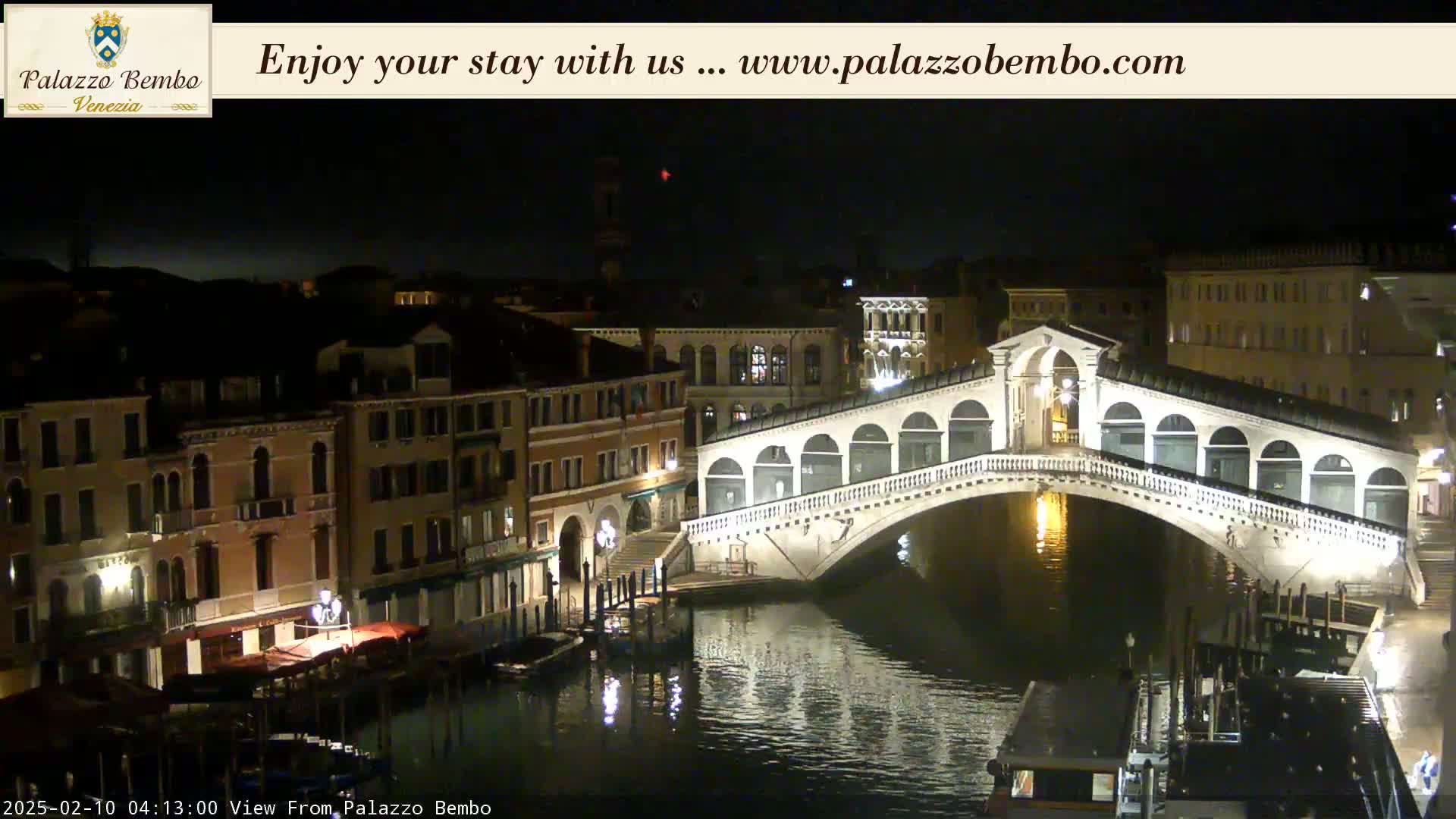 A nighttime view of a canal in Venice, showing a bridge illuminated against a dark sky.