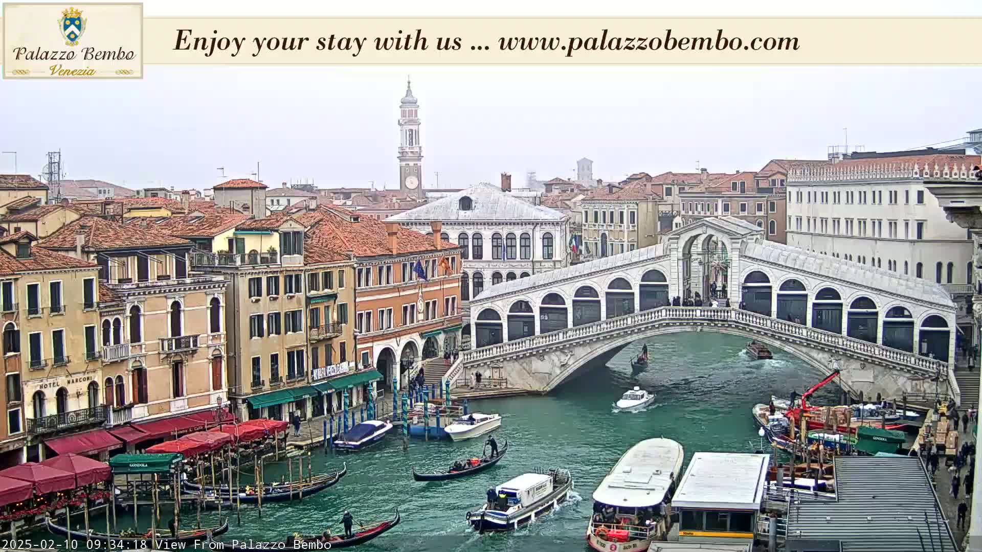 A view of a Venetian canal with gondolas, boats, and the Rialto Bridge on an overcast day.
