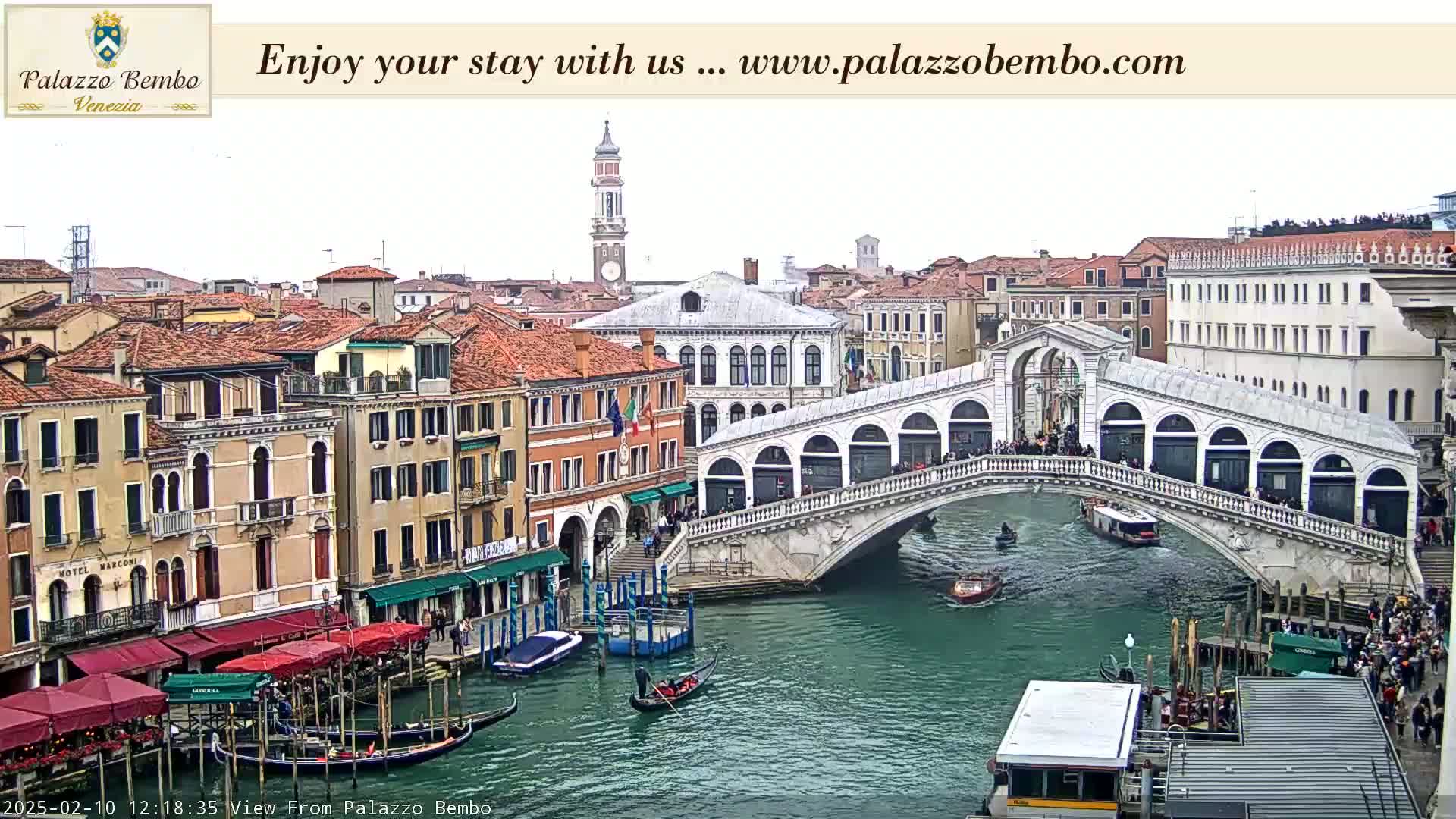 A canal in Venice, Italy, shows a stone bridge with people walking across it, gondolas in the water, and buildings lining the canal on a cloudy day.