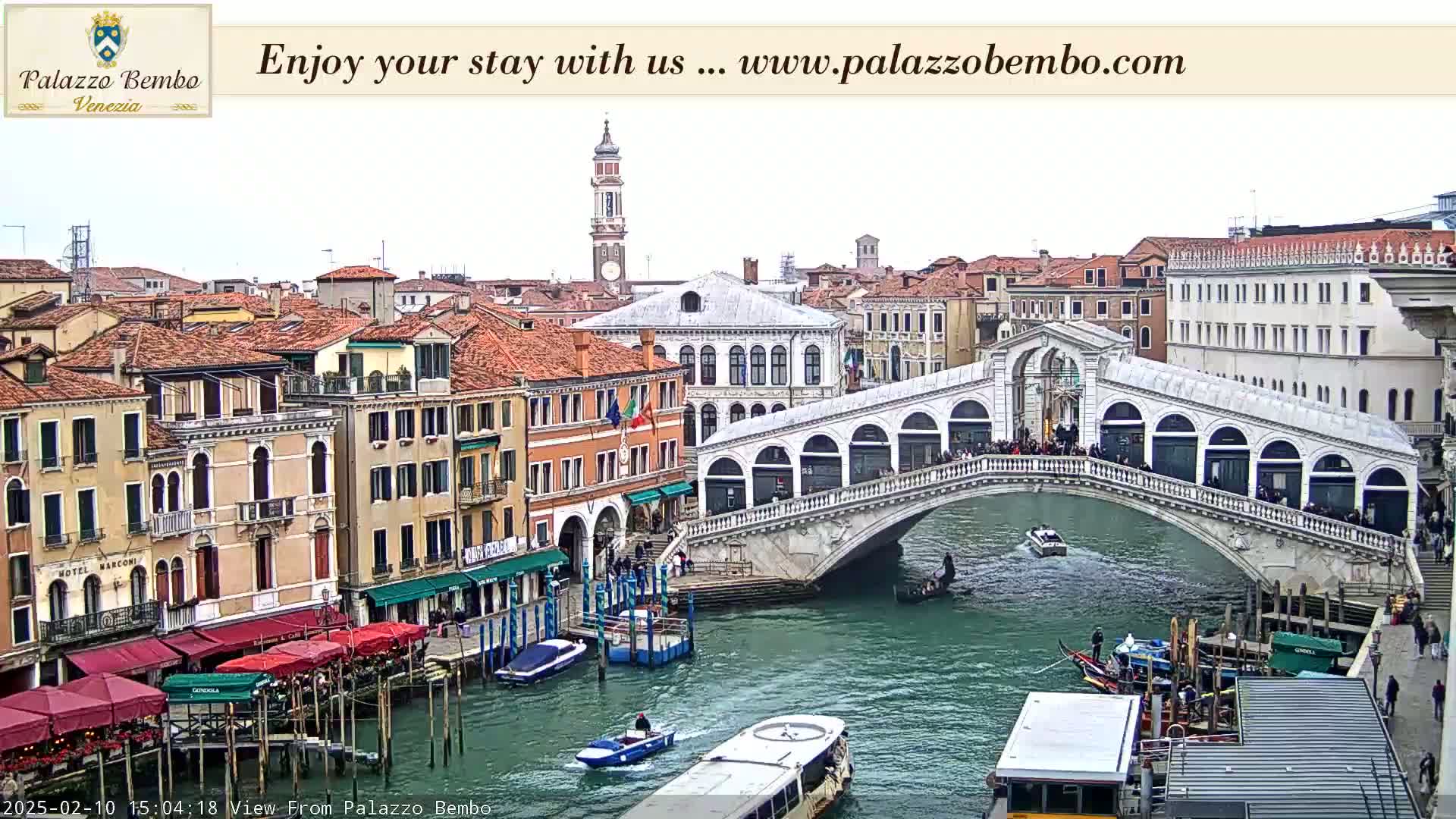 A view of the Rialto Bridge in Venice, Italy, on an overcast day, shows numerous gondolas and other boats on the canal below, with buildings lining the waterway.