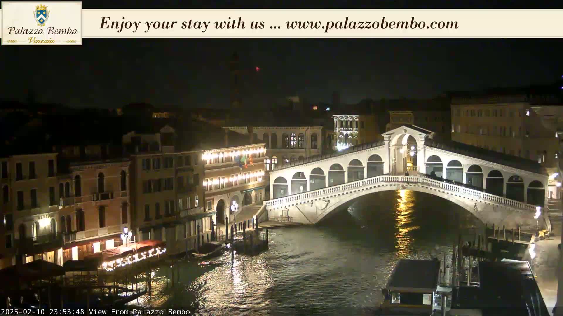 A nighttime view of a bridge over a canal in Venice, with buildings lit up along the waterway.