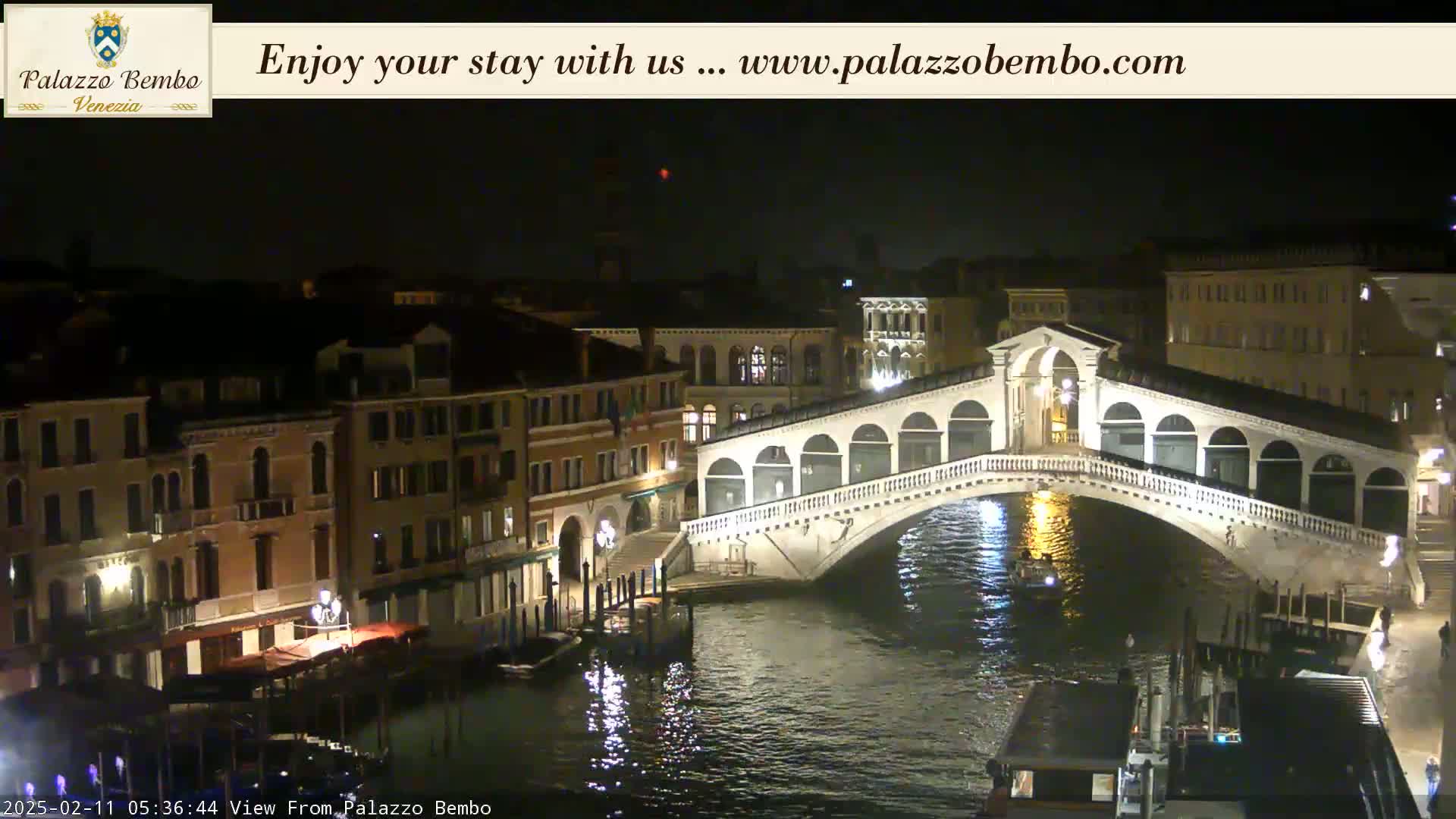 A nighttime view of a canal in Venice, showing the Ponte dei Sospiri and surrounding buildings illuminated under a clear, dark sky.