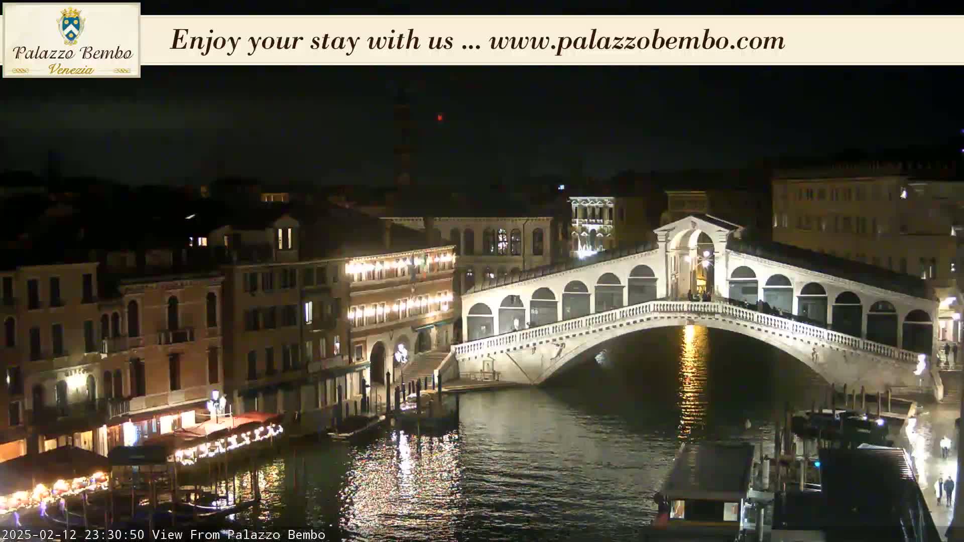 A nighttime view of a canal in Venice, showing a lit-up bridge and buildings along the water's edge under a clear, dark sky.