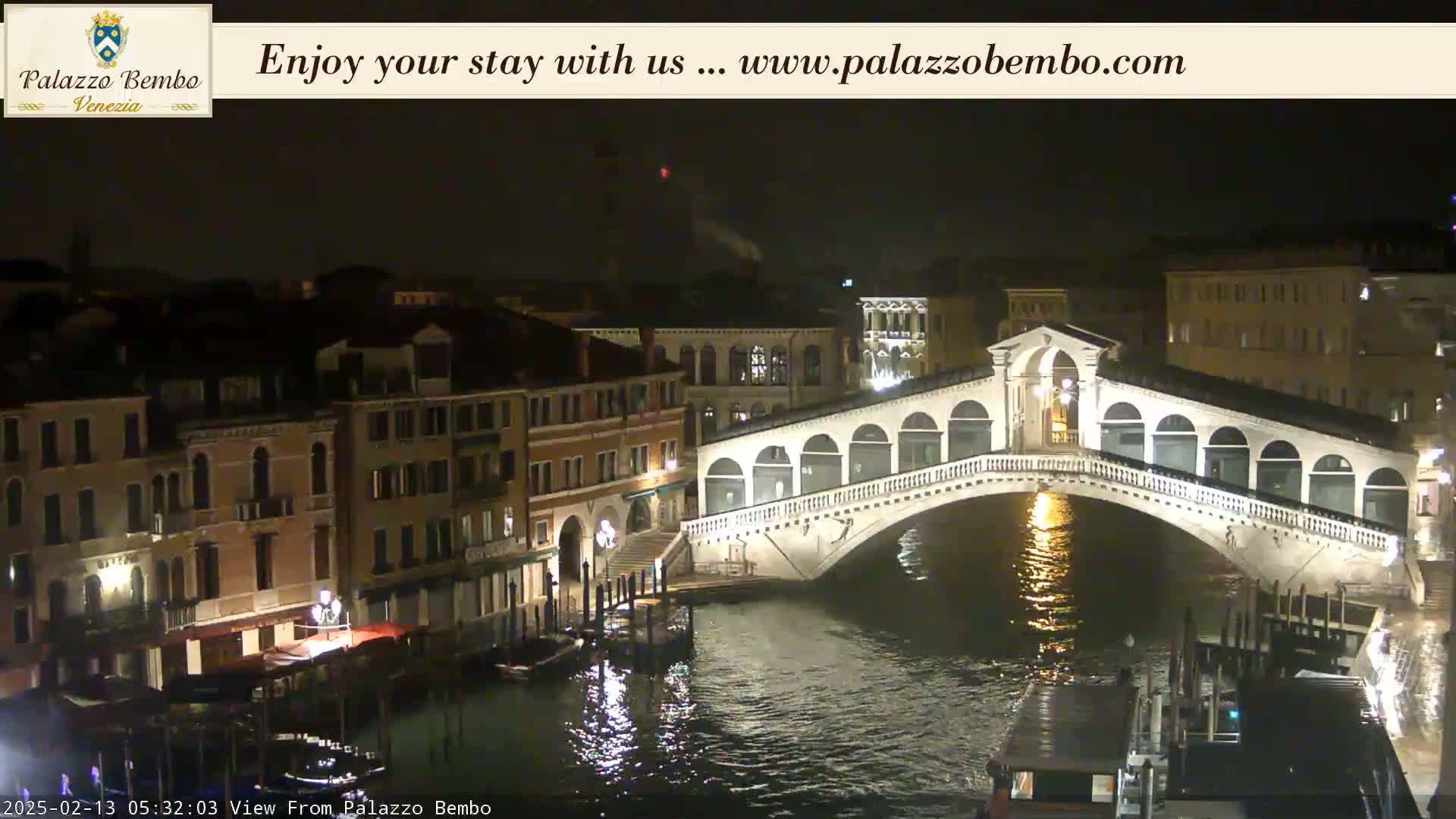 A nighttime view of a canal in Venice, showing a bridge and buildings illuminated along the waterway.