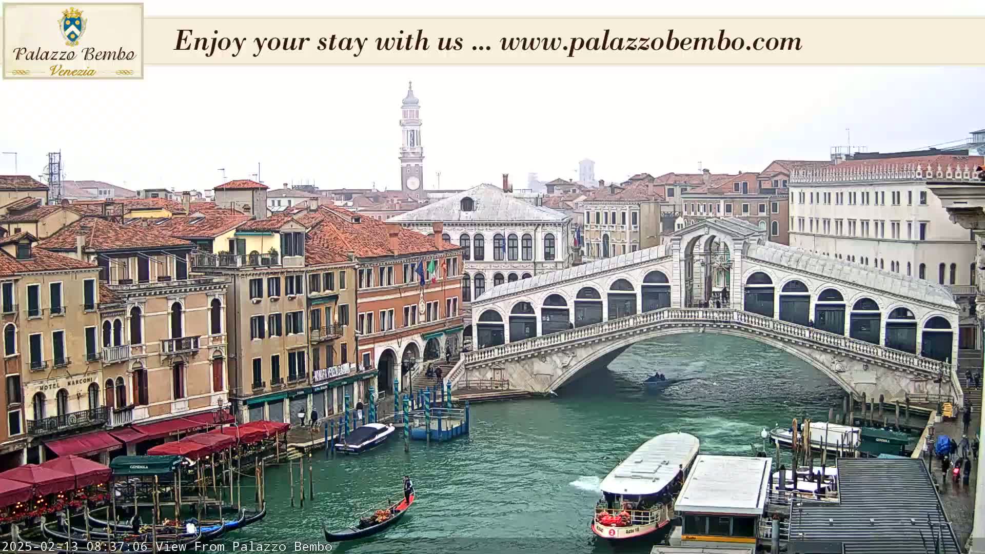 A canal in Venice, under an overcast sky, features a bridge with shops, boats, and several buildings along the waterway.
