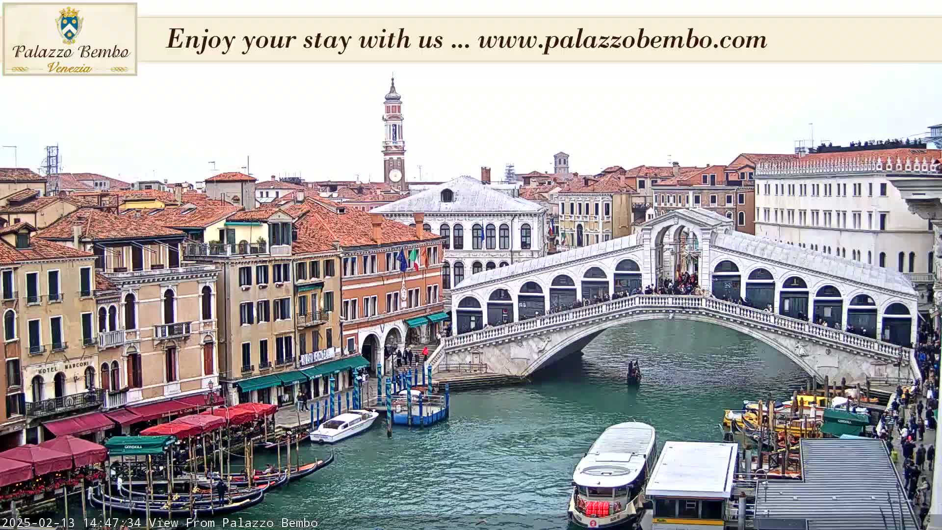 A view of the Rialto Bridge in Venice, Italy, with overcast skies, shows many boats on the canal and buildings along the waterway.