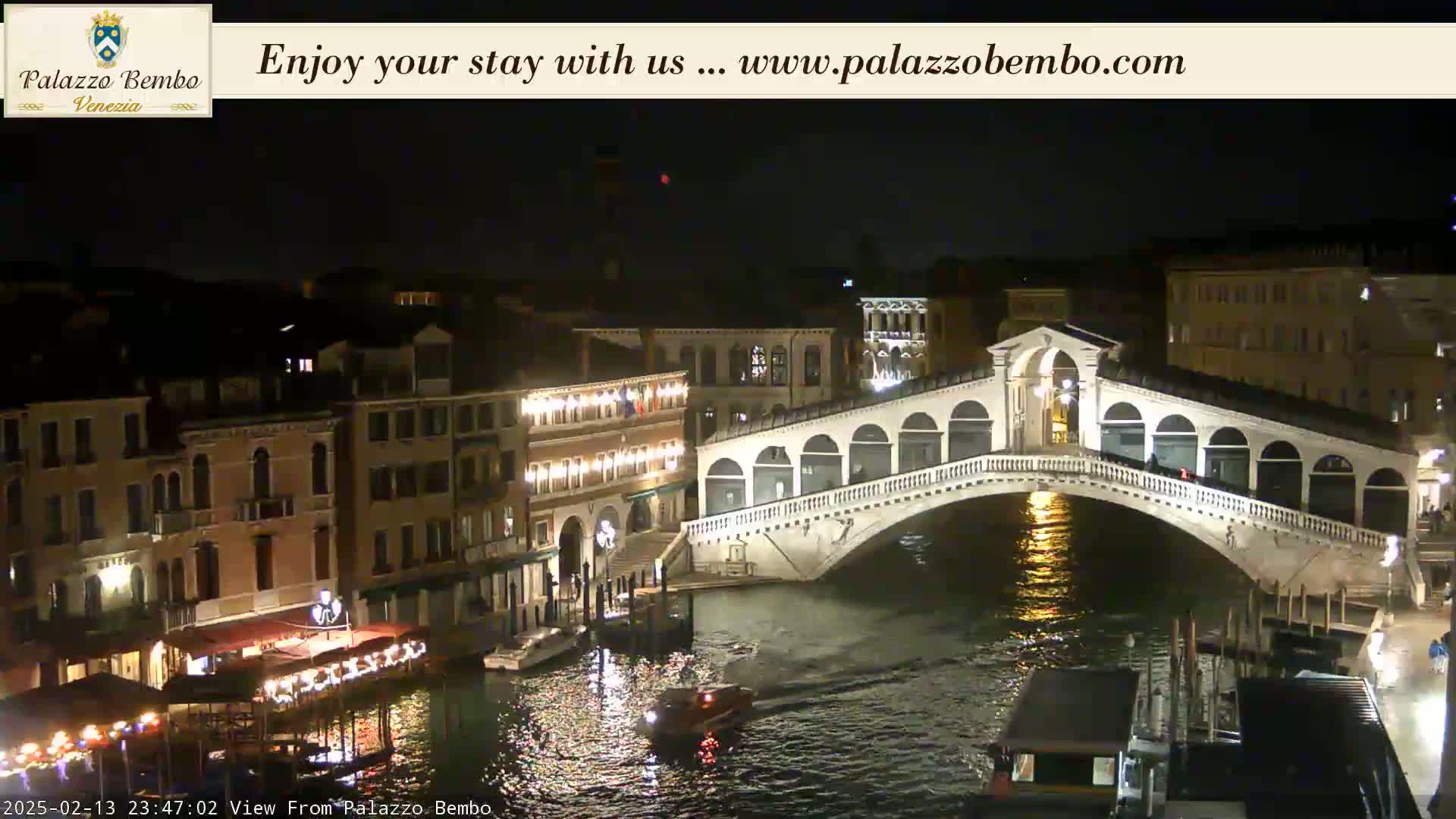 A nighttime view of a canal in Venice, showing a bridge illuminated against a dark sky.