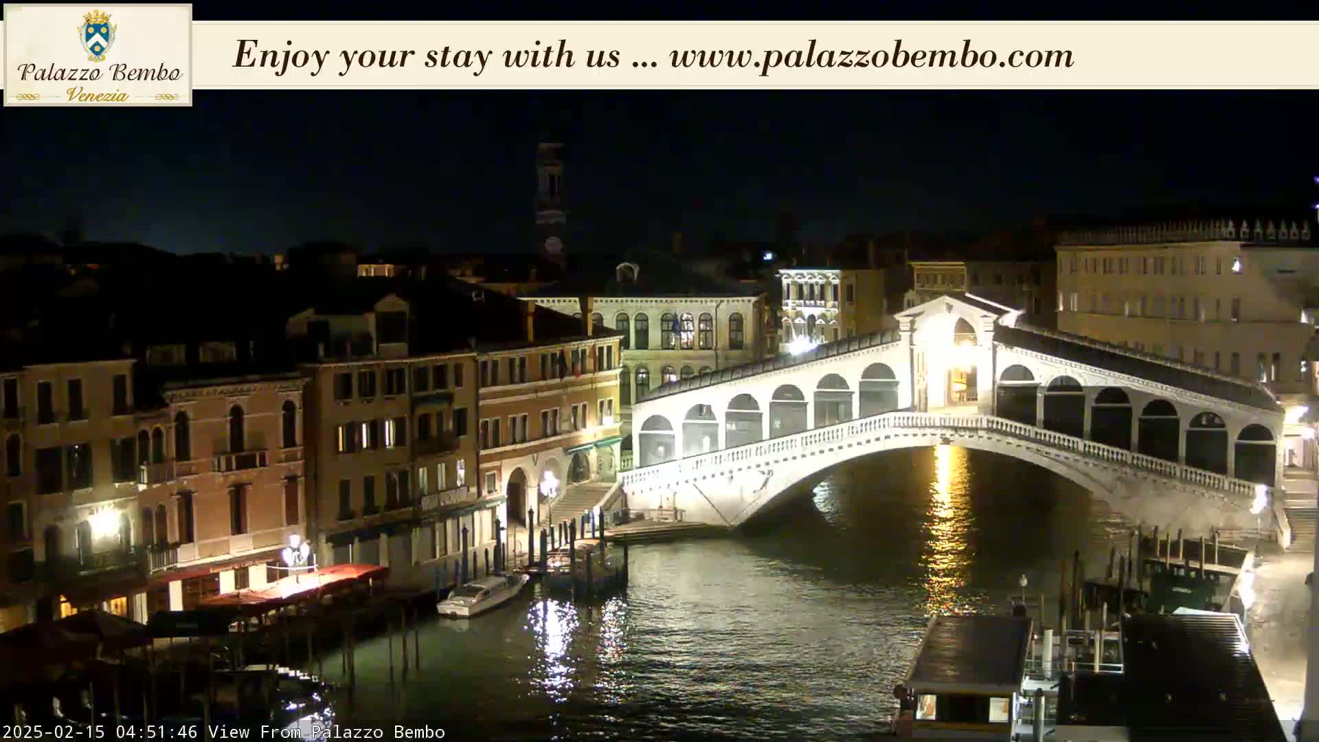 A nighttime view of a bridge over a canal in Venice, with illuminated buildings lining the waterway.