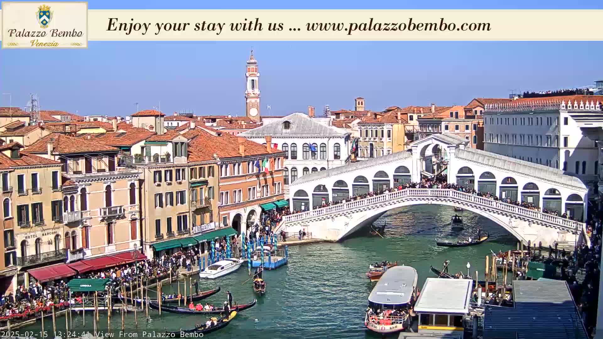 A sunny day in Venice shows a bustling canal scene with gondolas, boats, and many people walking across the Rialto Bridge.