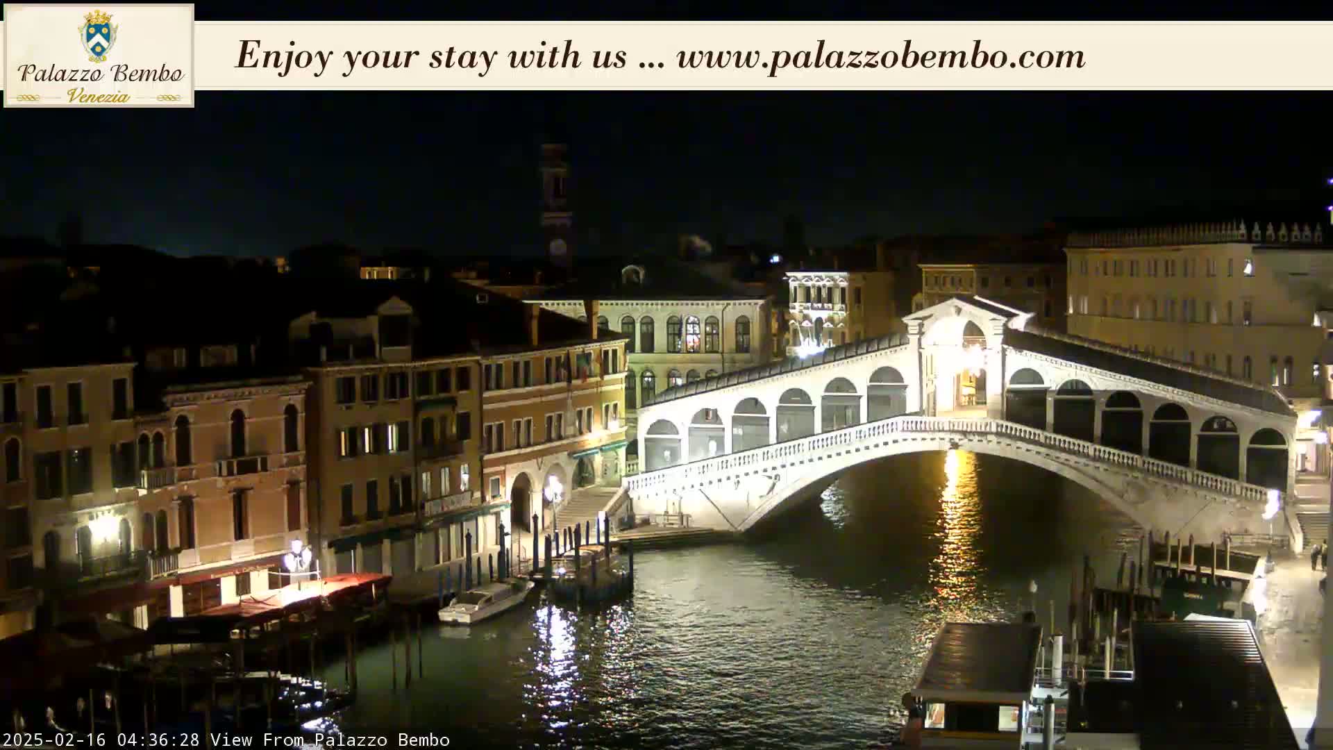 A nighttime view of a canal in Venice, showing a bridge lit up against a dark sky.