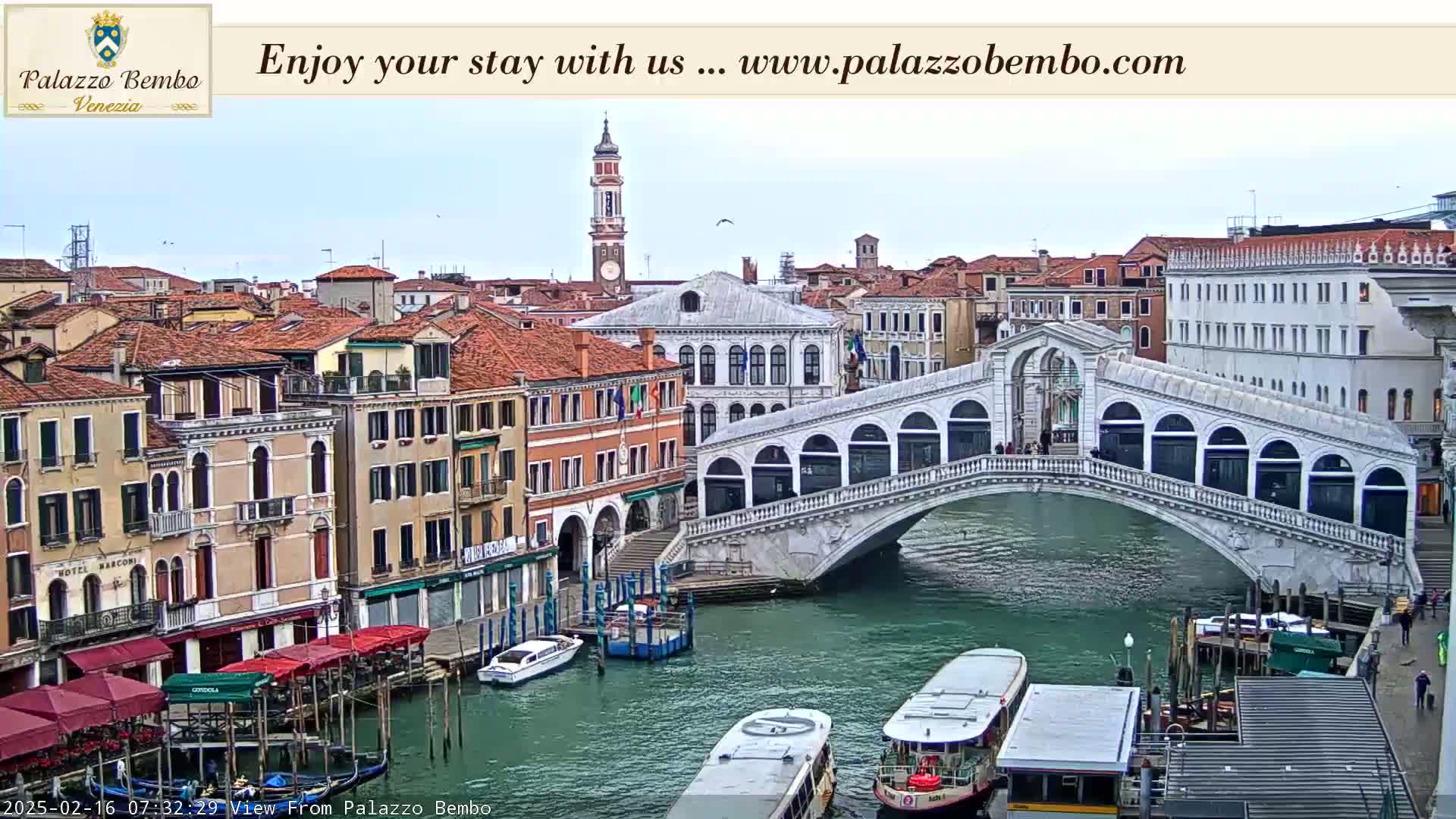 A view of a canal in Venice, under an overcast sky, shows a bridge, boats, and many buildings along the waterway.
