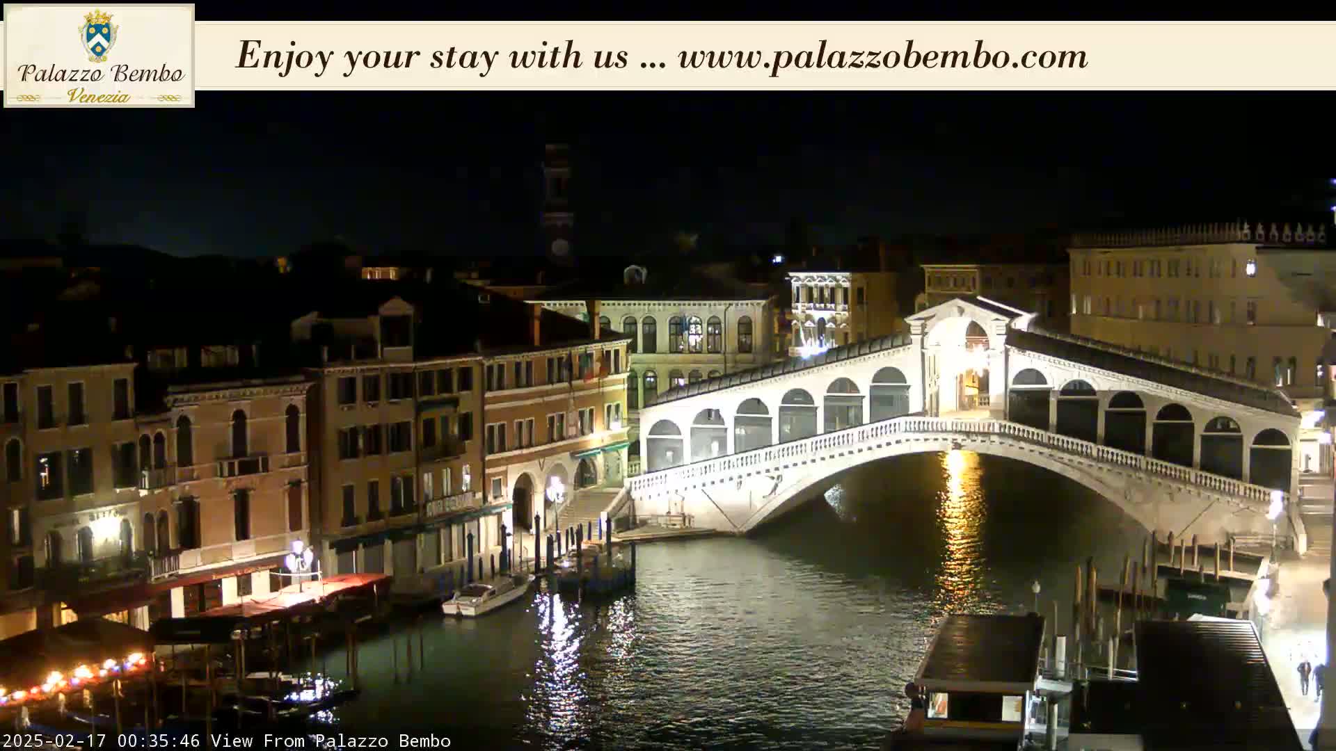 A nighttime view of a canal in Venice, showing a bridge lit up and buildings along the waterway under a clear, dark sky.