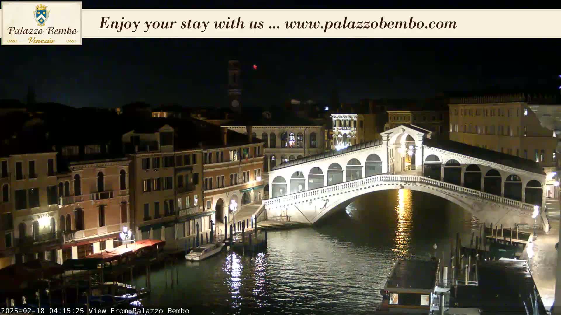 A nighttime view of a canal in Venice, showing a bridge and buildings illuminated by lights, with calm water reflecting the lights.