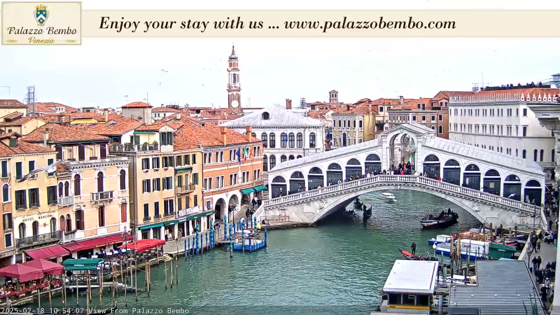 A view of a canal in Venice, with the Rialto Bridge in the foreground, under an overcast sky.