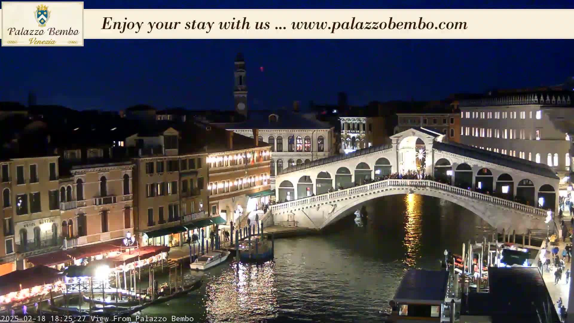 A nighttime view of a bridge over a canal in Venice, with illuminated buildings lining the waterway.