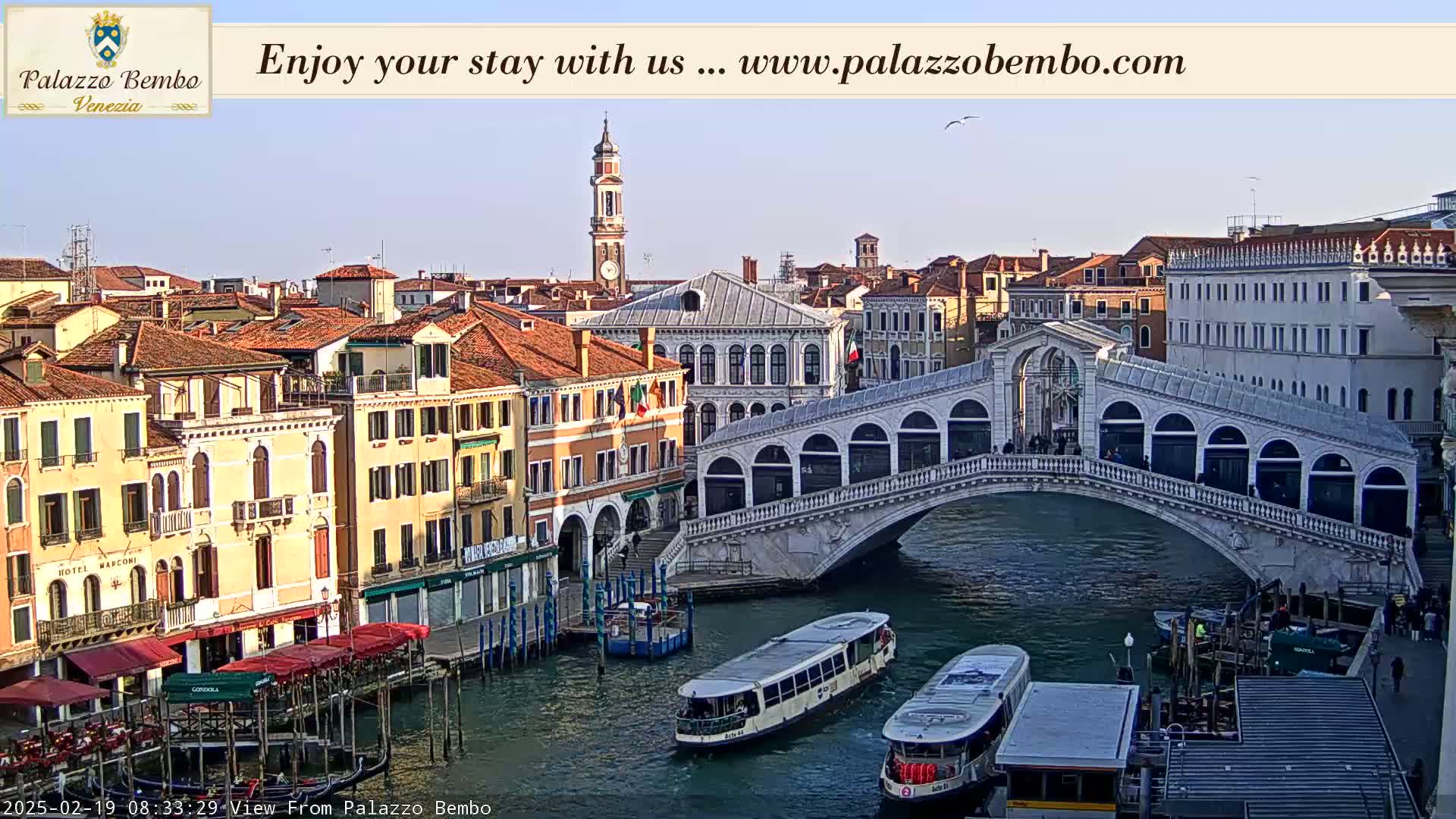 A sunny Venetian canal scene shows a bridge, boats, and numerous buildings along the waterfront.