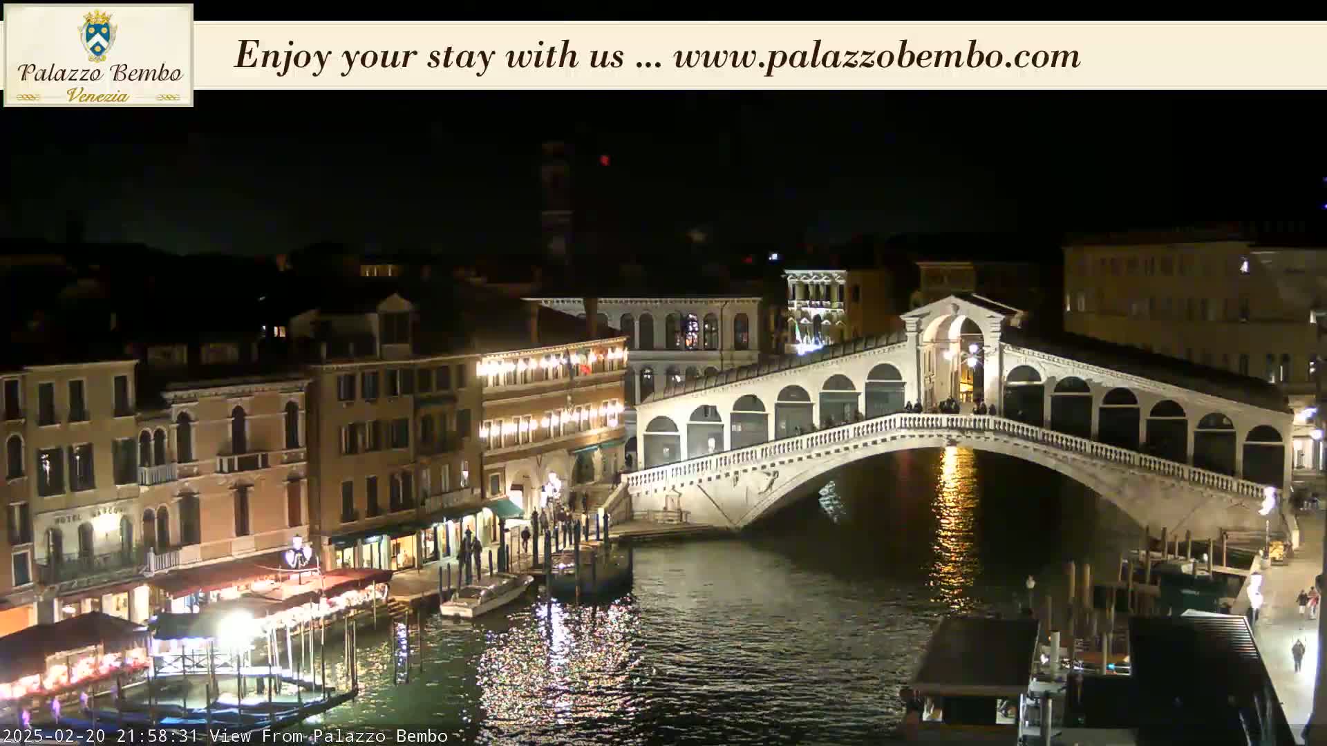 A nighttime view of a canal in Venice, with a bridge lit up and buildings along the water's edge.