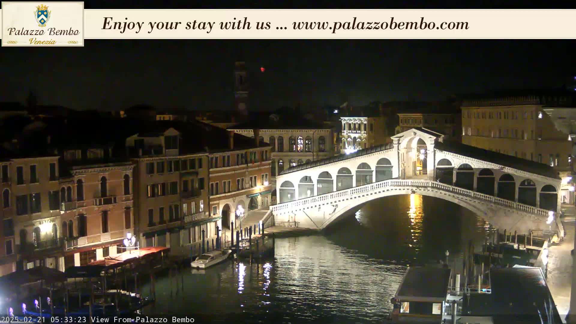 A nighttime view of a canal in Venice, showing a bridge with lights and buildings along the waterway.