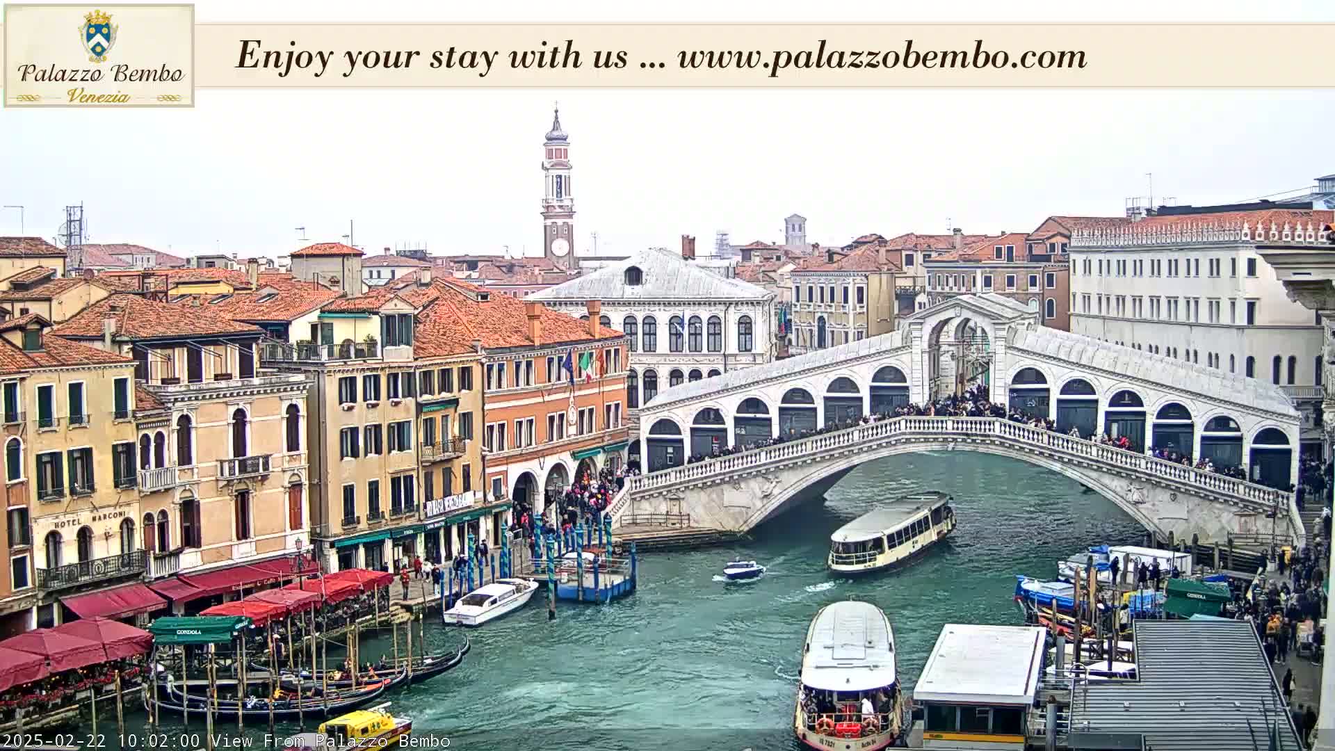 A Venetian canal scene shows the Rialto Bridge crowded with people, numerous boats, and buildings lining the waterway under an overcast sky.