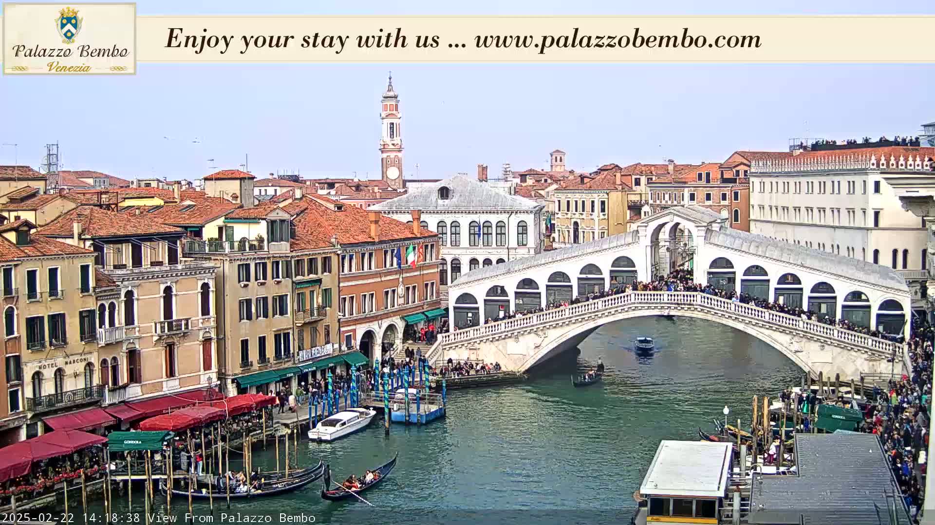 A sunny day in Venice shows the Rialto Bridge crowded with people, gondolas in the canal below, and colorful buildings lining the waterway.