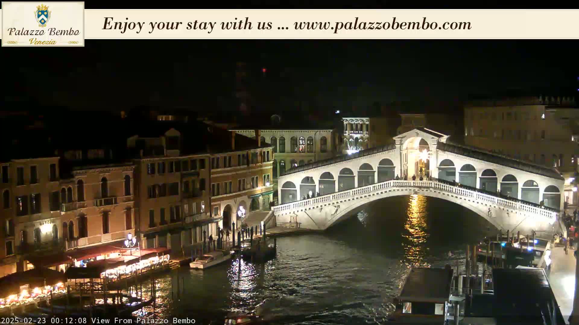 A nighttime view of a bridge spanning a canal in Venice, with buildings illuminated along the waterway.