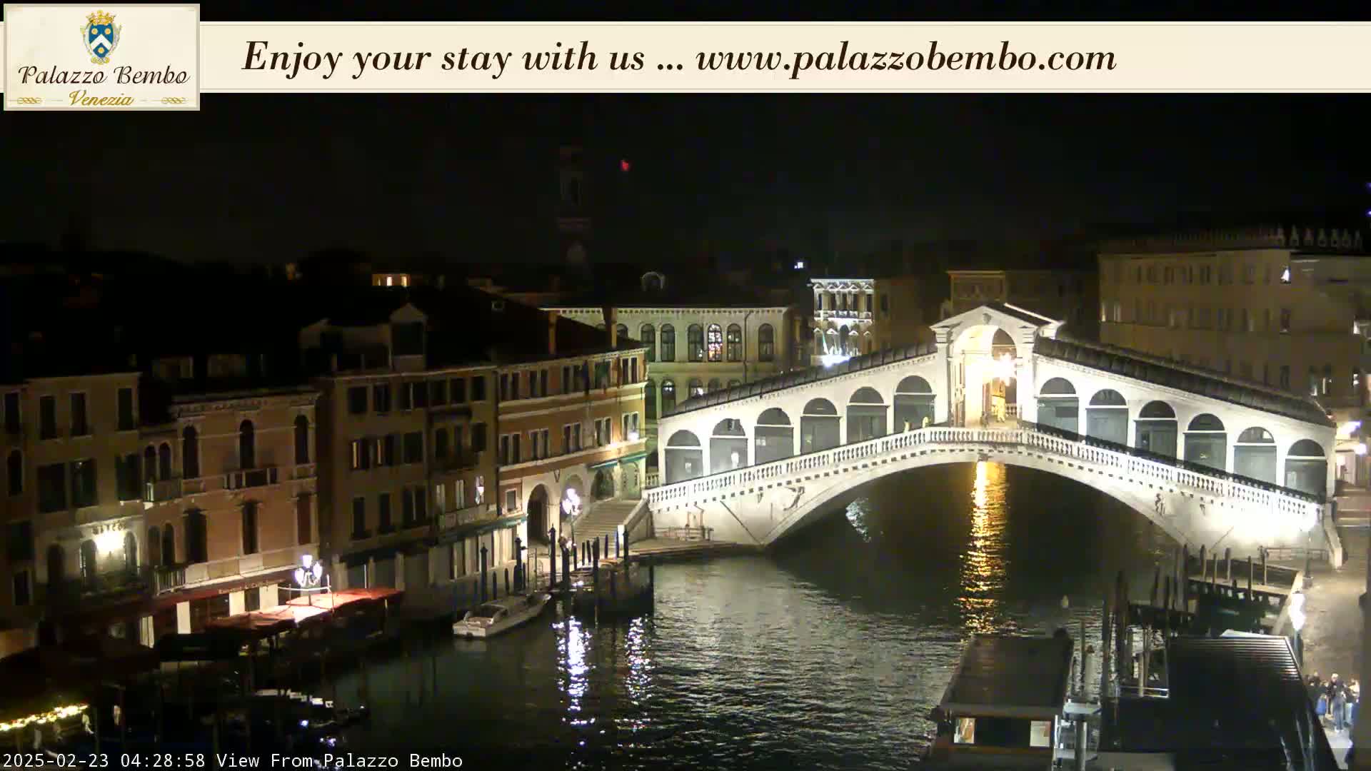 A nighttime view of a bridge over a canal in Venice, with illuminated buildings lining the waterway.