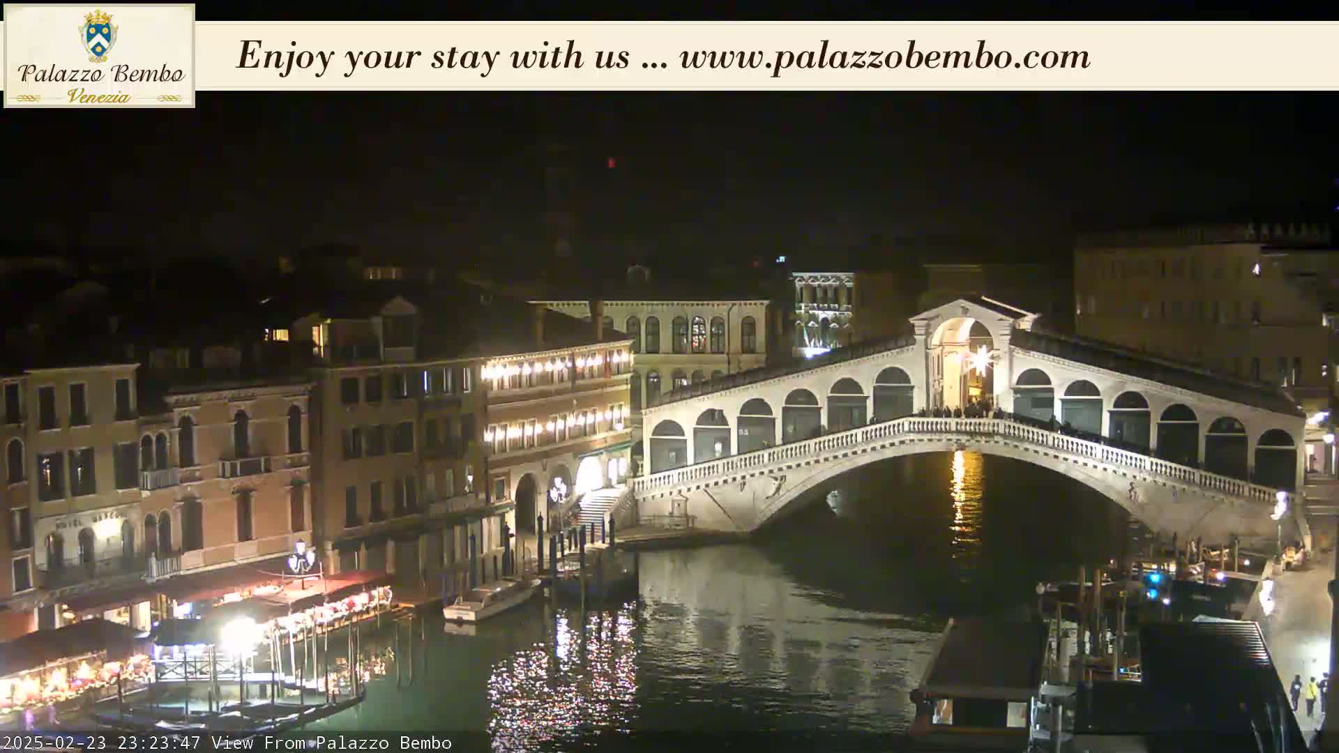 A nighttime view of a bridge spanning a canal in Venice, with buildings illuminated along the waterway.