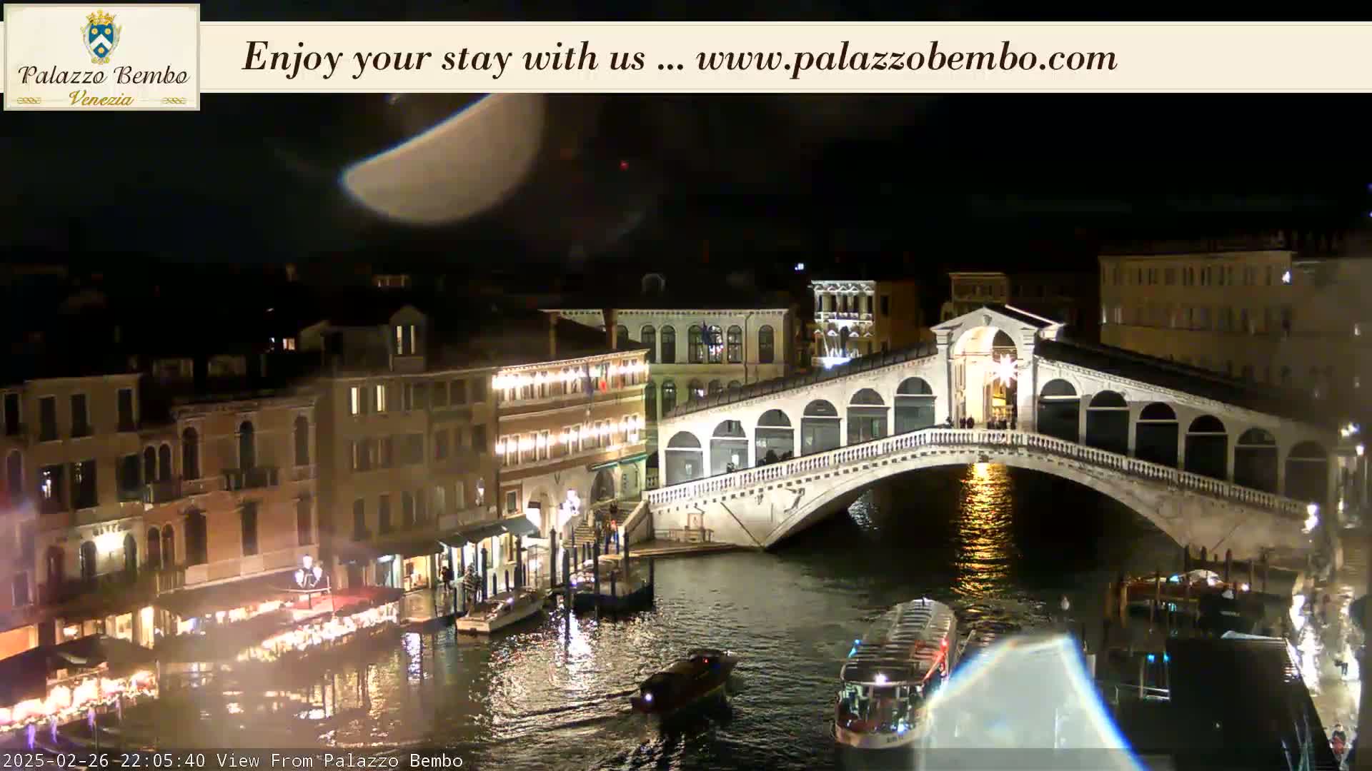 A nighttime view of a bridge spanning a canal in Venice, with buildings lit up along the waterway under a clear sky.