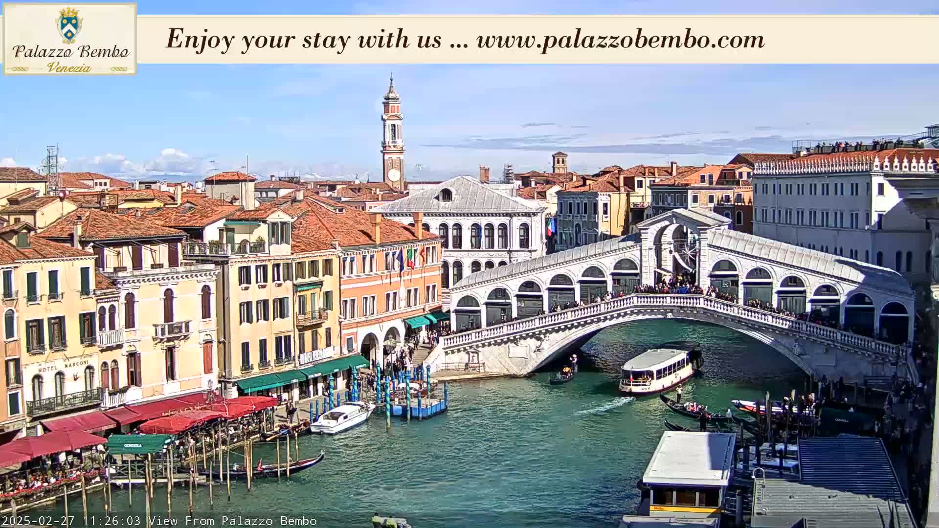 A sunny day in Venice shows a canal with gondolas and a bridge crowded with people, alongside colorful buildings.