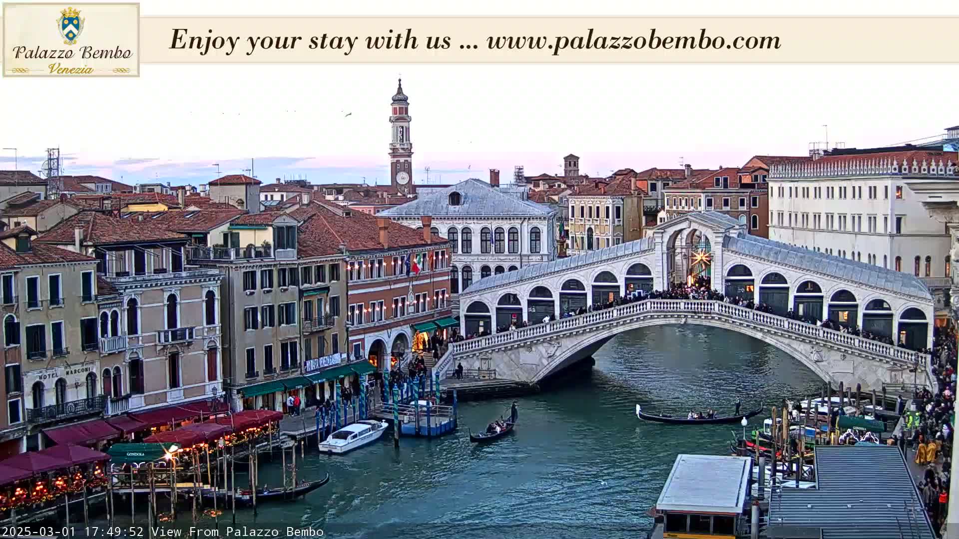 A Venetian bridge at dusk, with gondolas on the canal below and buildings lining the waterway.