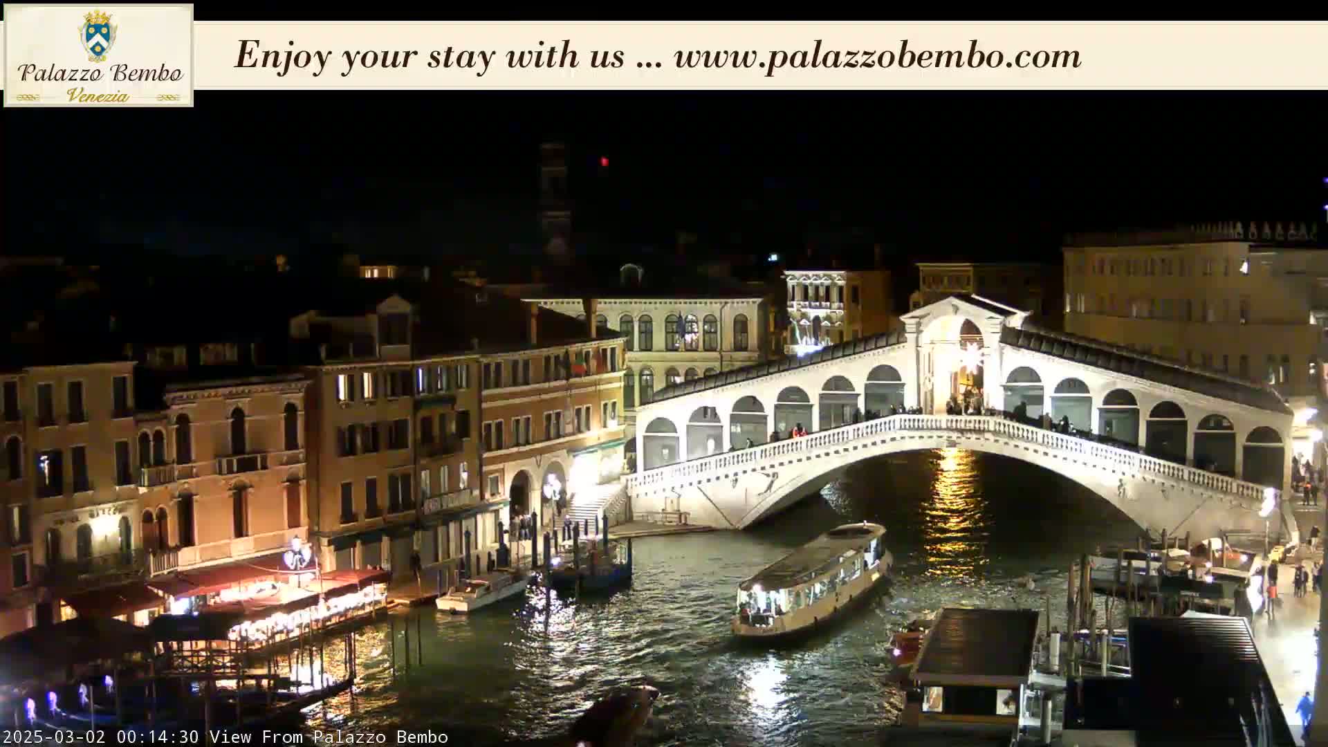 A nighttime view of a bridge over a canal in Venice, with buildings illuminated along the waterway.
