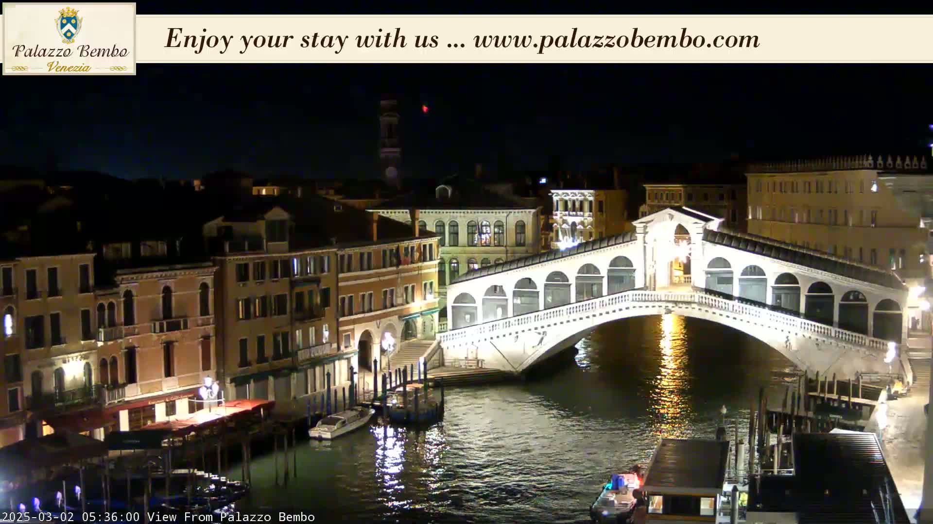 A nighttime view of a canal in Venice, showing a bridge illuminated against a dark sky.