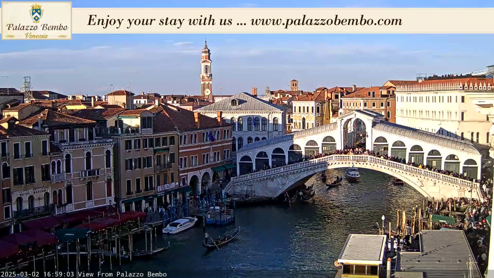 A sunny Venetian canal scene shows a crowded bridge arching over the water, with numerous gondolas and buildings lining the waterway.