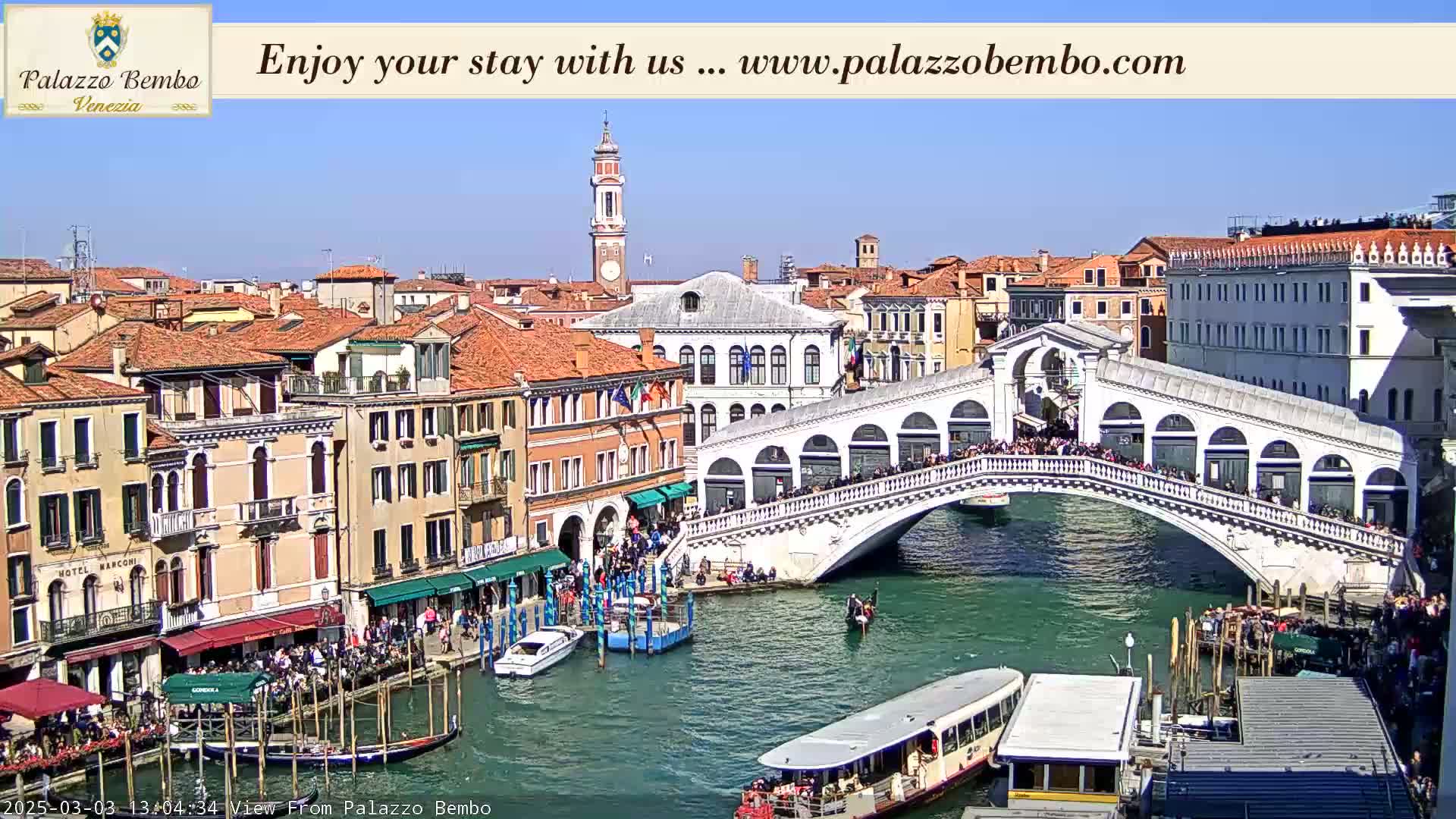 A sunny day in Venice shows a canal with boats and gondolas, crowded with people, and the Rialto Bridge spanning the waterway, with buildings lining both sides.