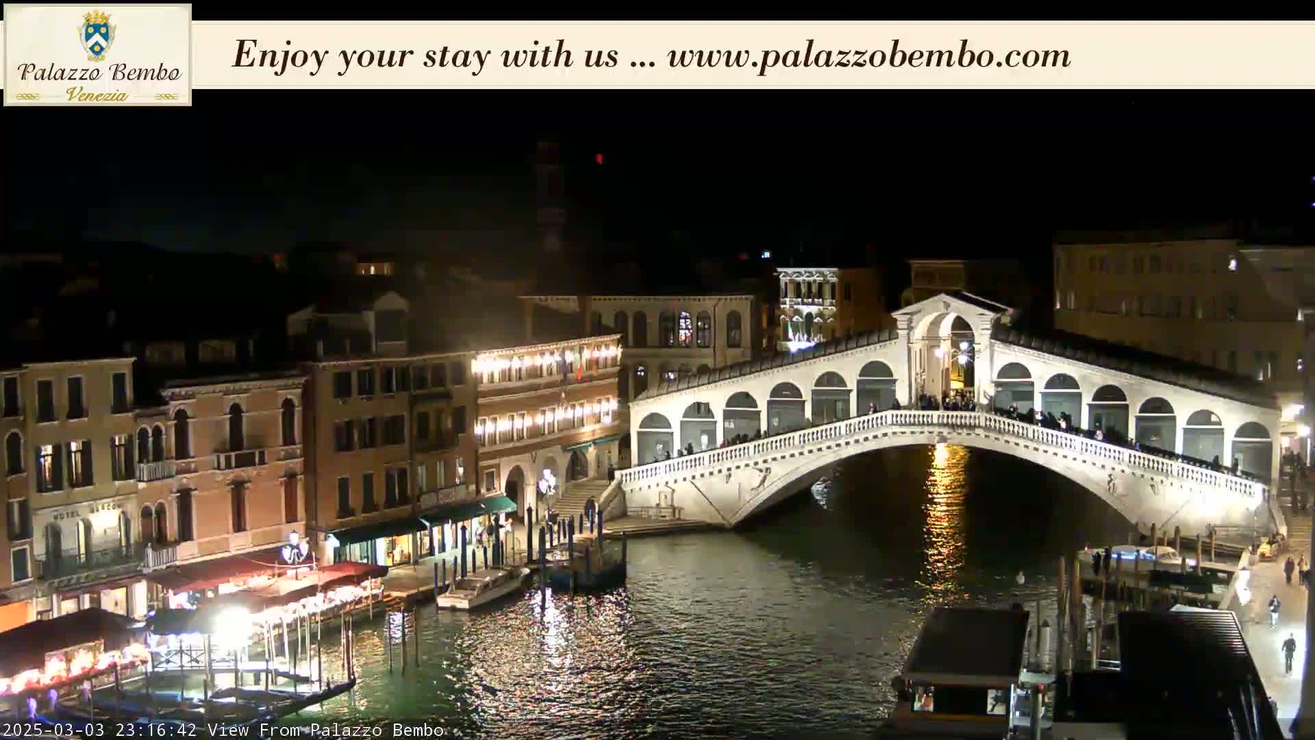 At night, a lit bridge spans a canal lined with illuminated buildings in Venice.