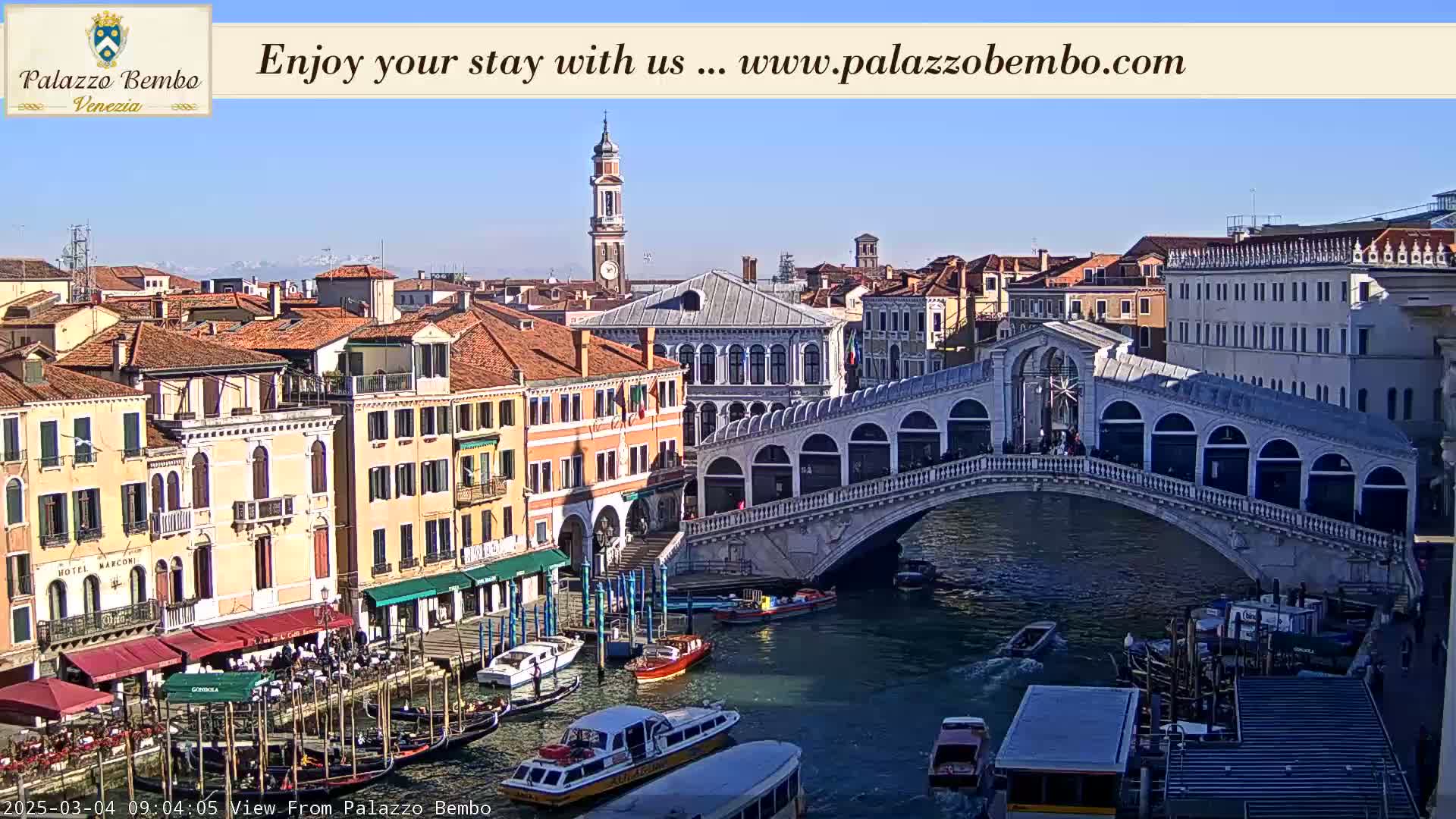 A sunny day in Venice shows a canal with gondolas and boats under the Rialto Bridge, surrounded by historic buildings.