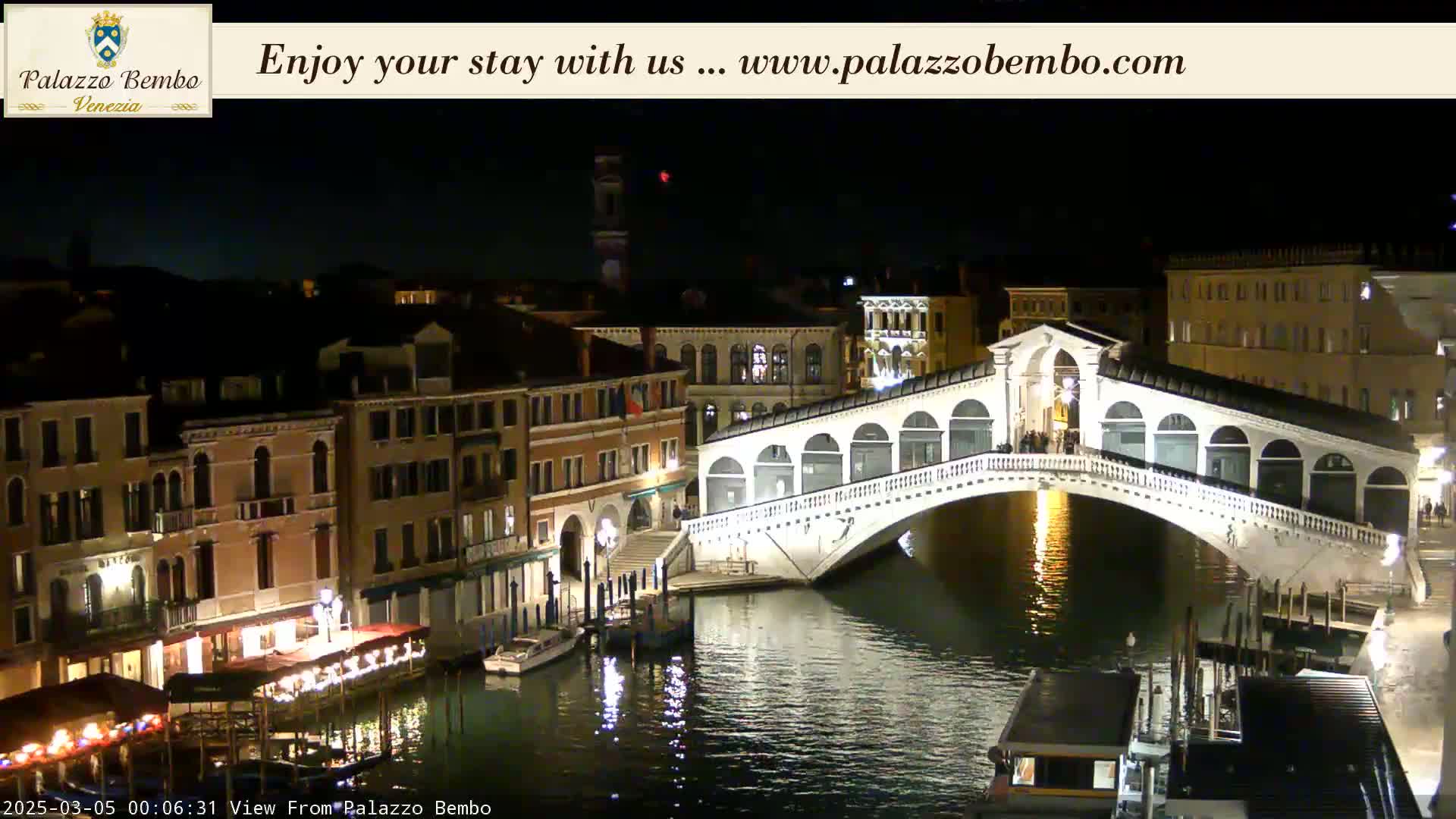 A nighttime view of a canal in Venice, showing a bridge illuminated against a dark sky.