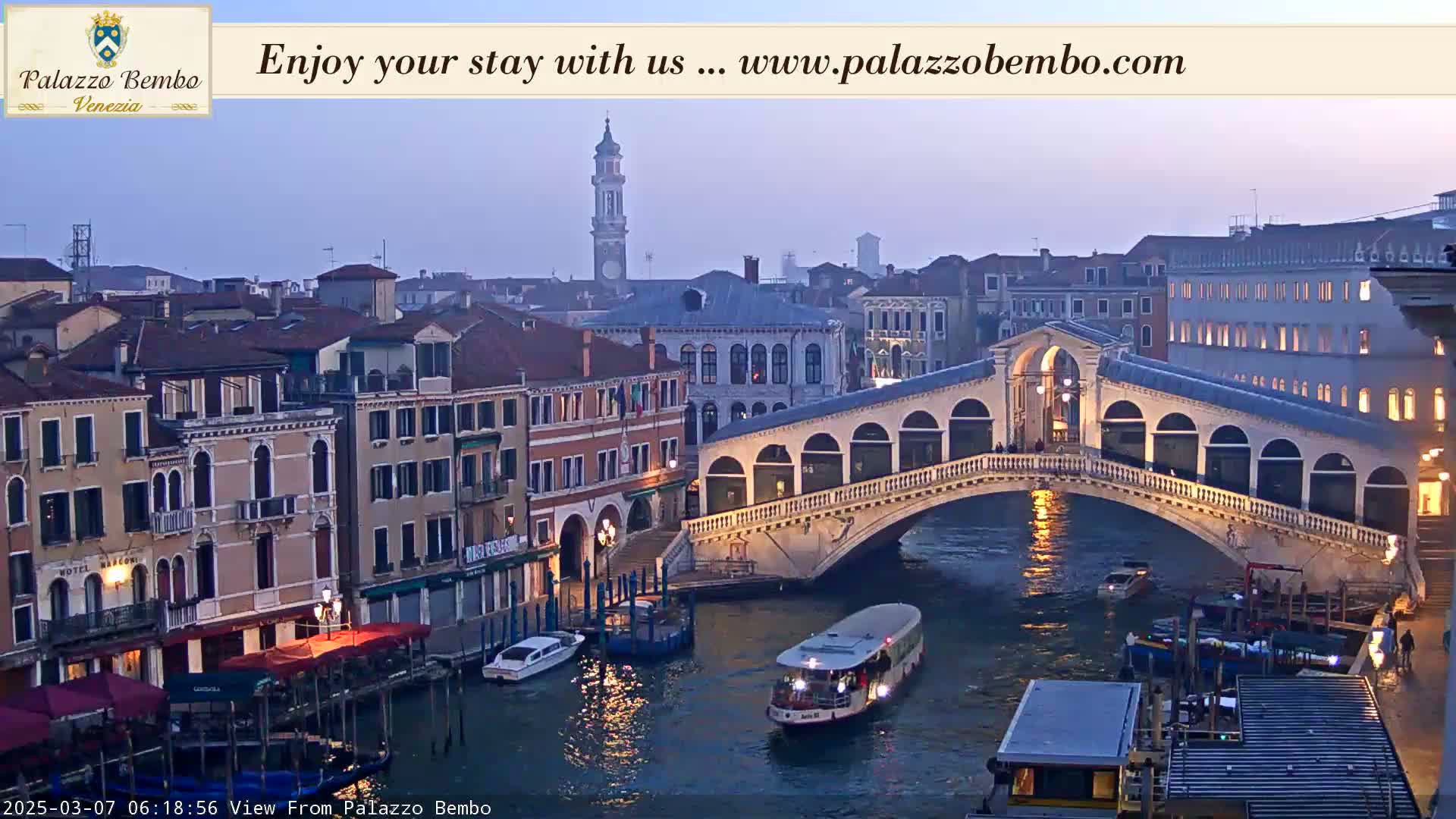 A Venetian canal at dusk, showing a bridge and colorful buildings along the waterway, with boats on the water.