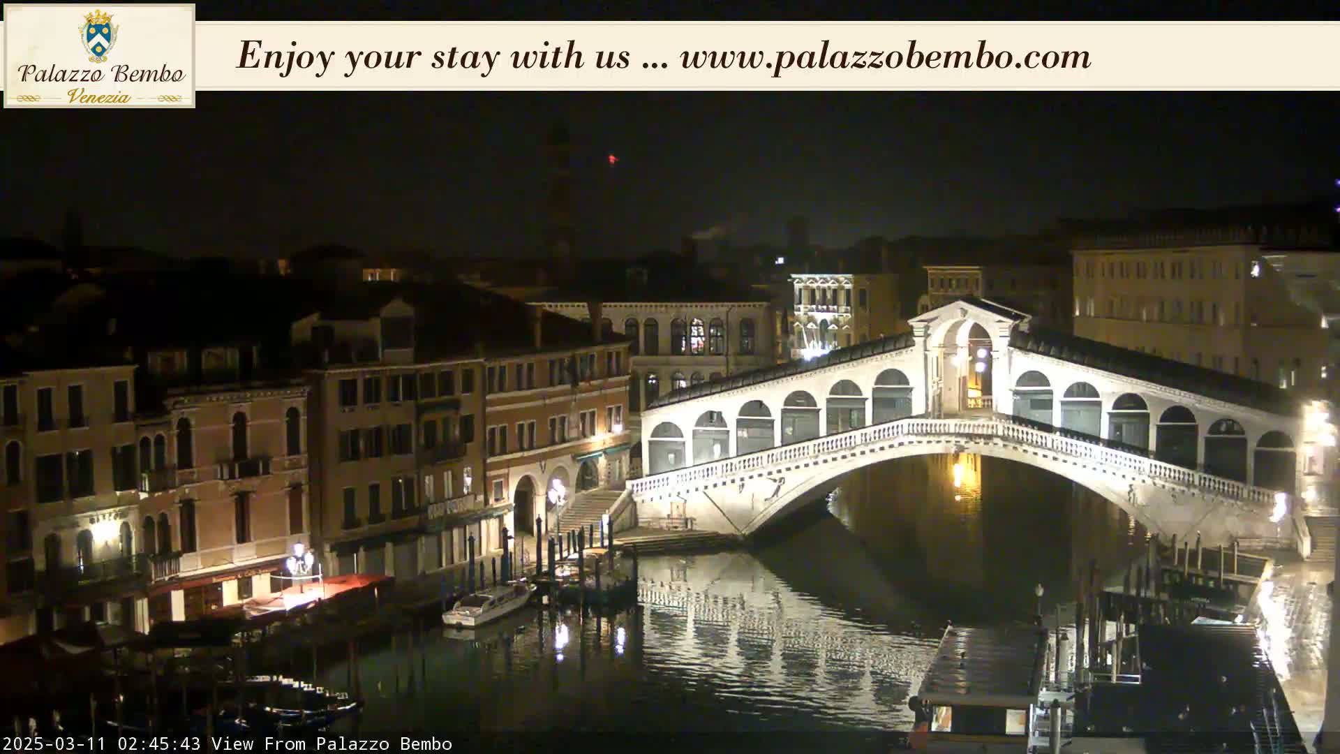 A nighttime view of a canal in Venice, with a bridge illuminated and buildings lining the waterway.