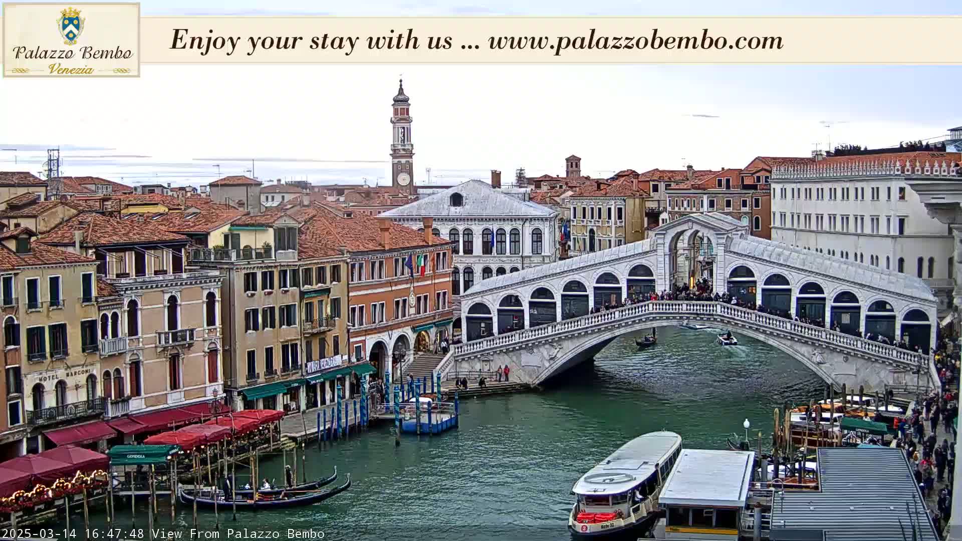 A Venetian canal scene under a mostly cloudy sky shows the Rialto Bridge crowded with people, gondolas, and water taxis.