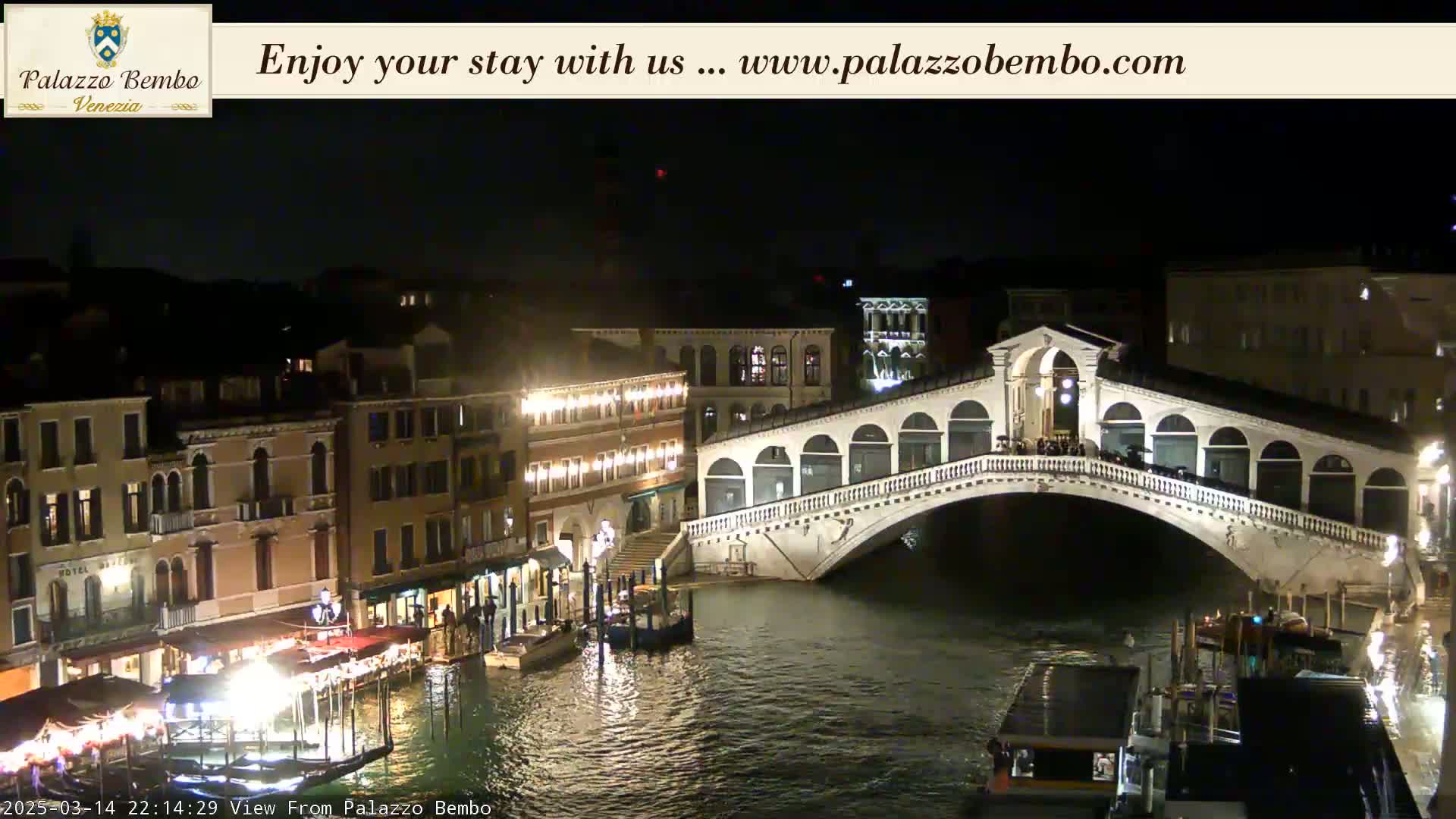 A nighttime view of a bridge over a canal in Venice, with buildings illuminated along the waterway.