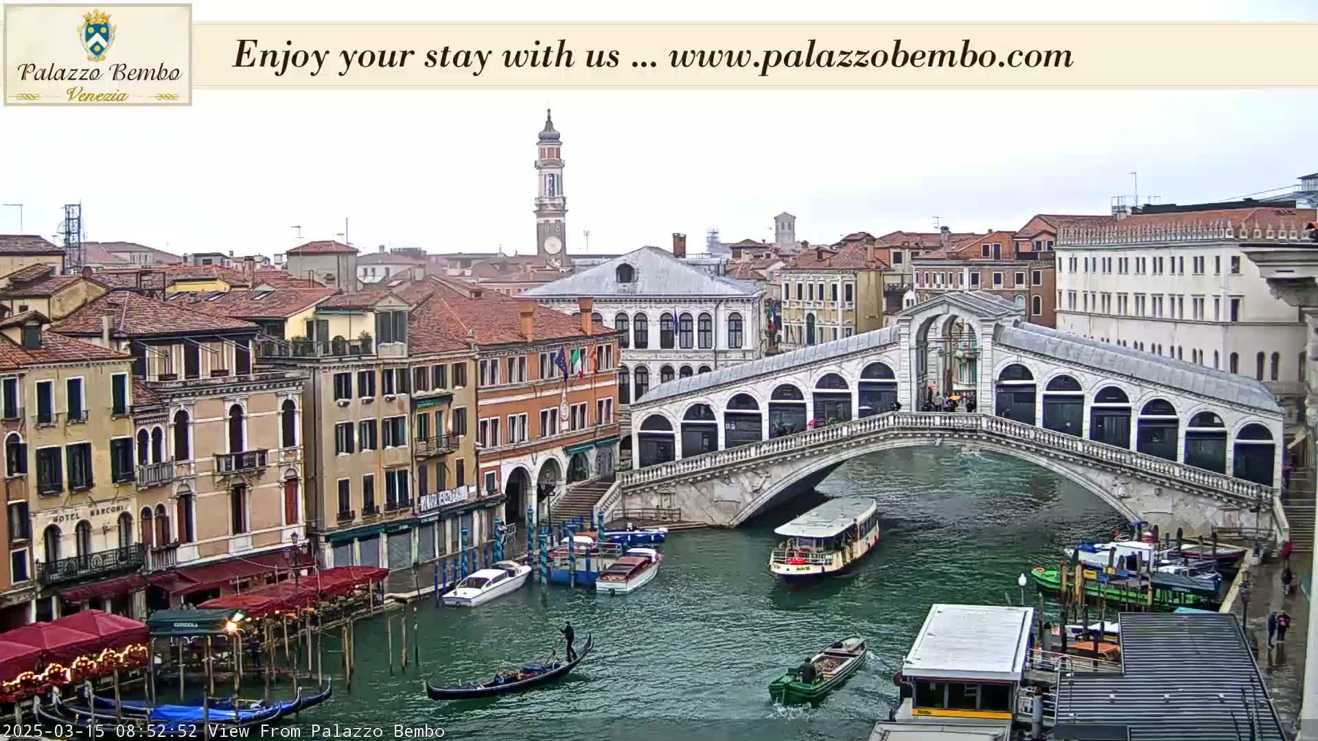 A view of a canal in Venice, Italy, on an overcast day, showing several buildings, a bridge, gondolas, and water taxis.