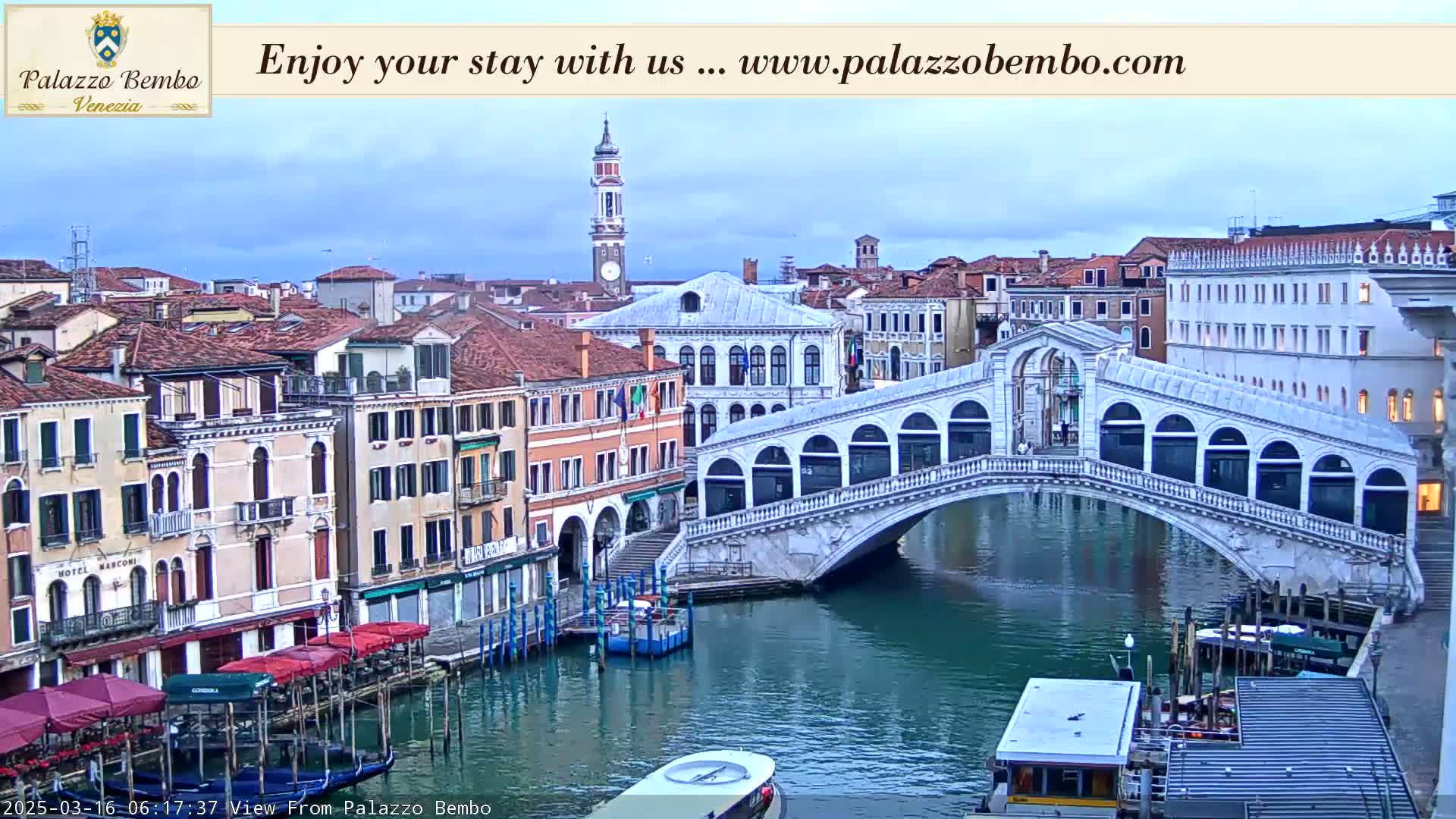 A view of a canal in Venice, under a partly cloudy sky, shows a bridge, several buildings, and boats.