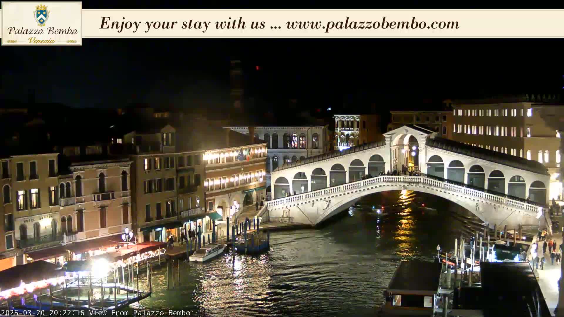 A nighttime view of a bridge over a canal in Venice, with illuminated buildings lining the waterway.