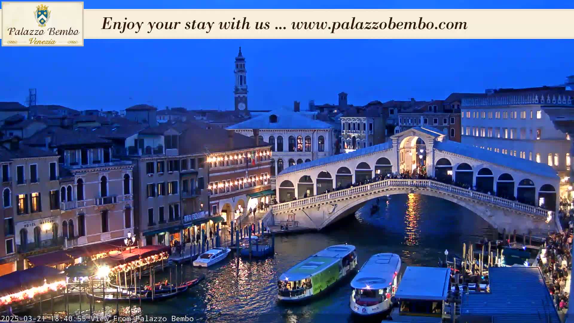 A twilight view of a Venetian bridge spanning a canal, with boats and buildings lining the waterway.