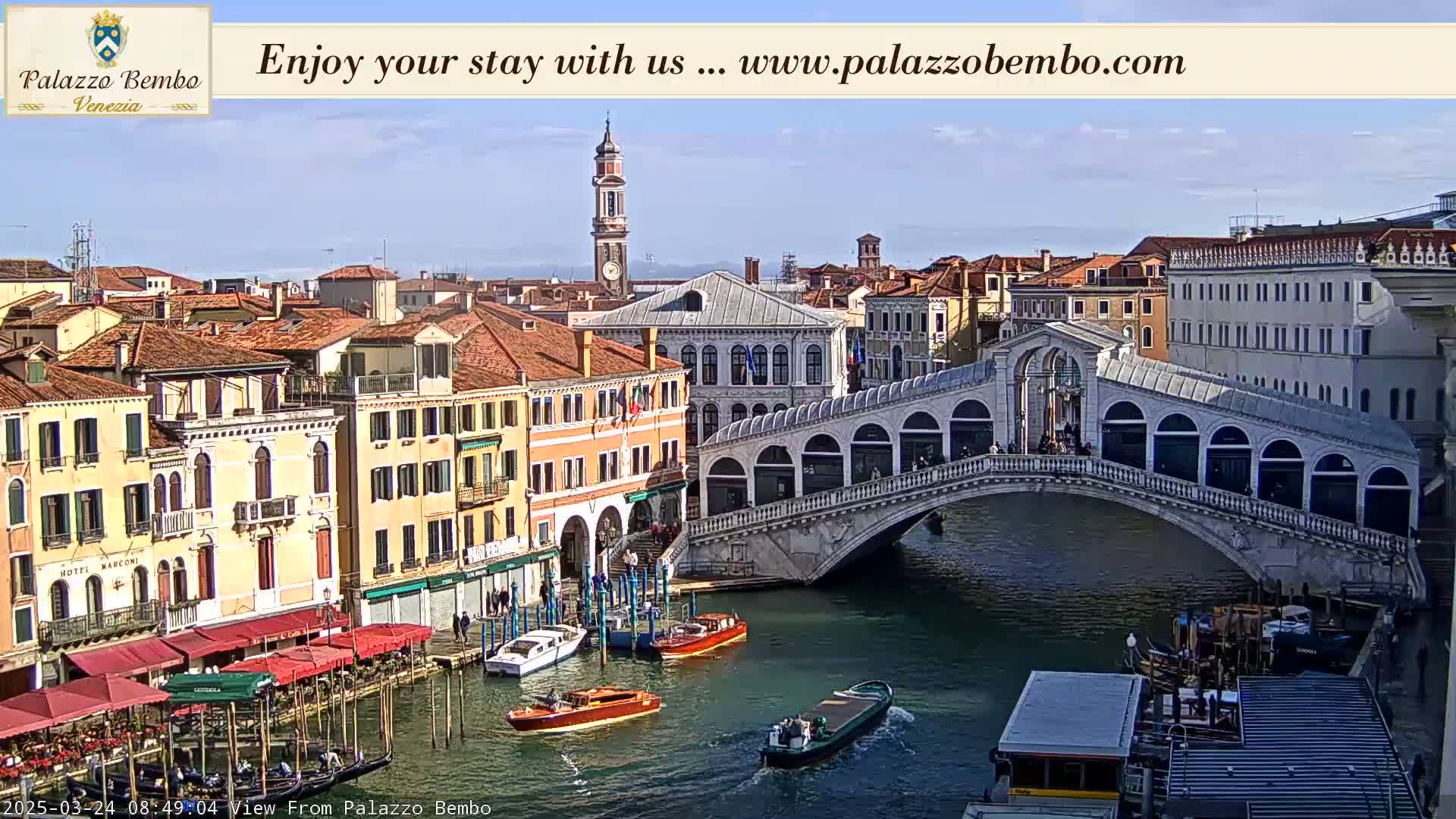 A sunny day in Venice shows a canal with boats and gondolas, alongside buildings and the Rialto Bridge.