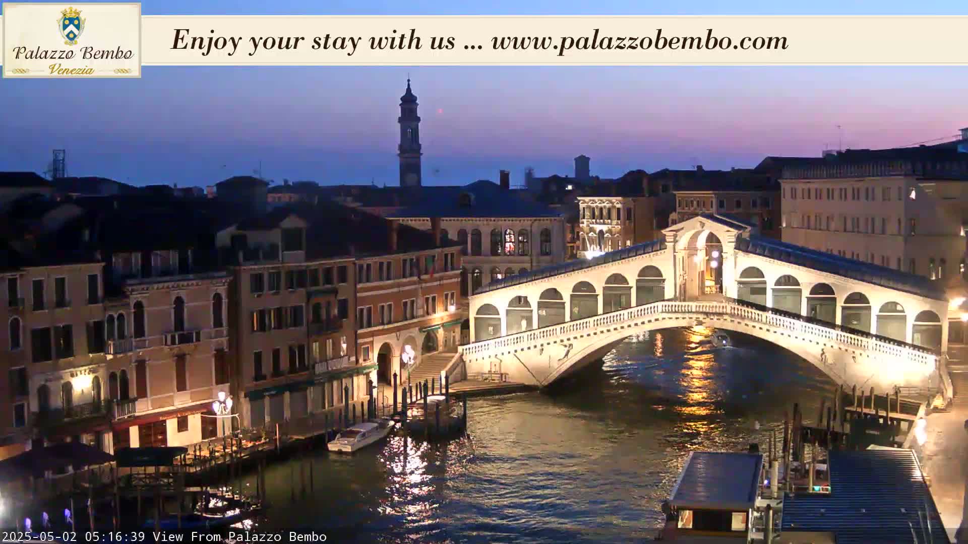 A twilight view of a lit bridge spanning a canal in Venice, with buildings lining the waterway.