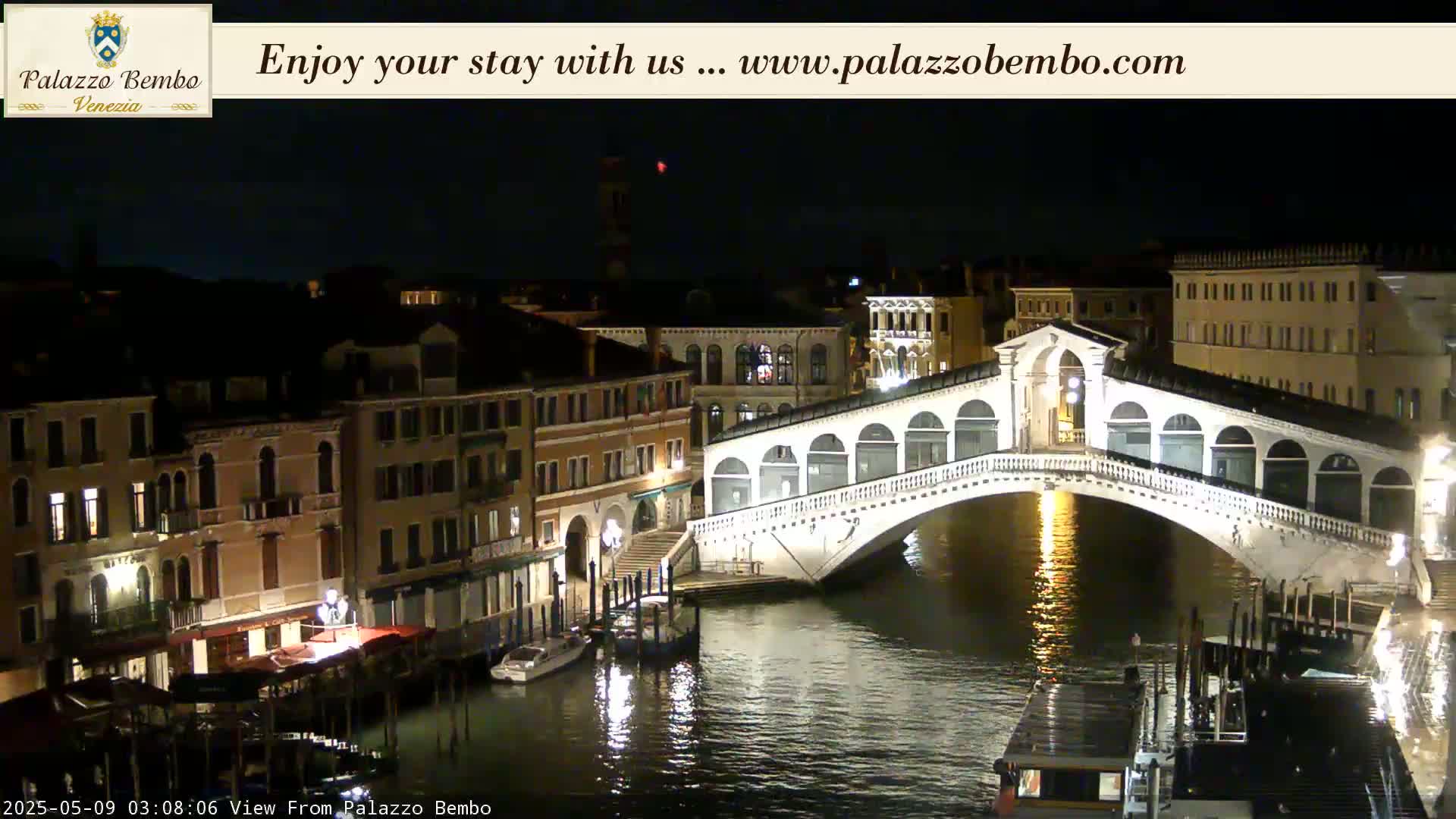 A brightly lit bridge arches over a dark canal in a city at night.